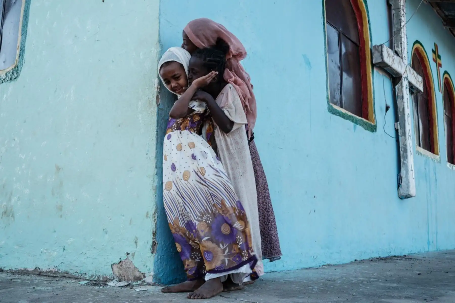 Los niños miran desde detrás de la esquina de un edificio de la iglesia construido por ex refugiados etíopes, mientras los fieles locales y refugiados asisten a la misa dominical en la aldea junto al campo de refugiados de Um Raquba en Gedaref, en el este de Sudán. Foto: AFP