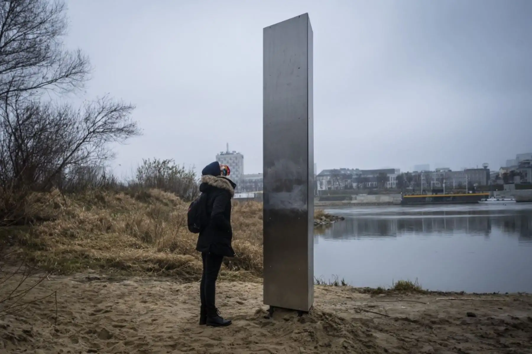 Una mujer mira el 10 de diciembre de 2020 un monolito de metal que ha aparecido en la orilla del Vístula en la capital polaca, Varsovia, el último de una serie de objetos similares que han aparecido recientemente en Europa y Estados Unidos. Foto: AFP