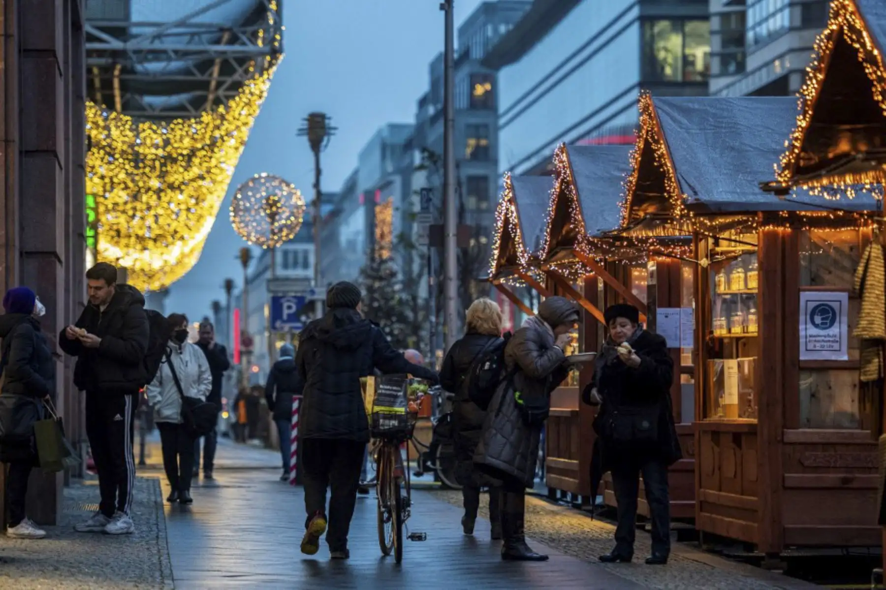 La gente come bocadillos comprados en los puestos navideños en la Friedrichstrasse de Berlín. Las autoridades locales han permitido una cantidad limitada de puestos de temporada que venden especialidades navideñas después de que se cancelaran los tradicionales mercados navideños debido a la pandemia del Coronavirus covid-19. Foto: AFP