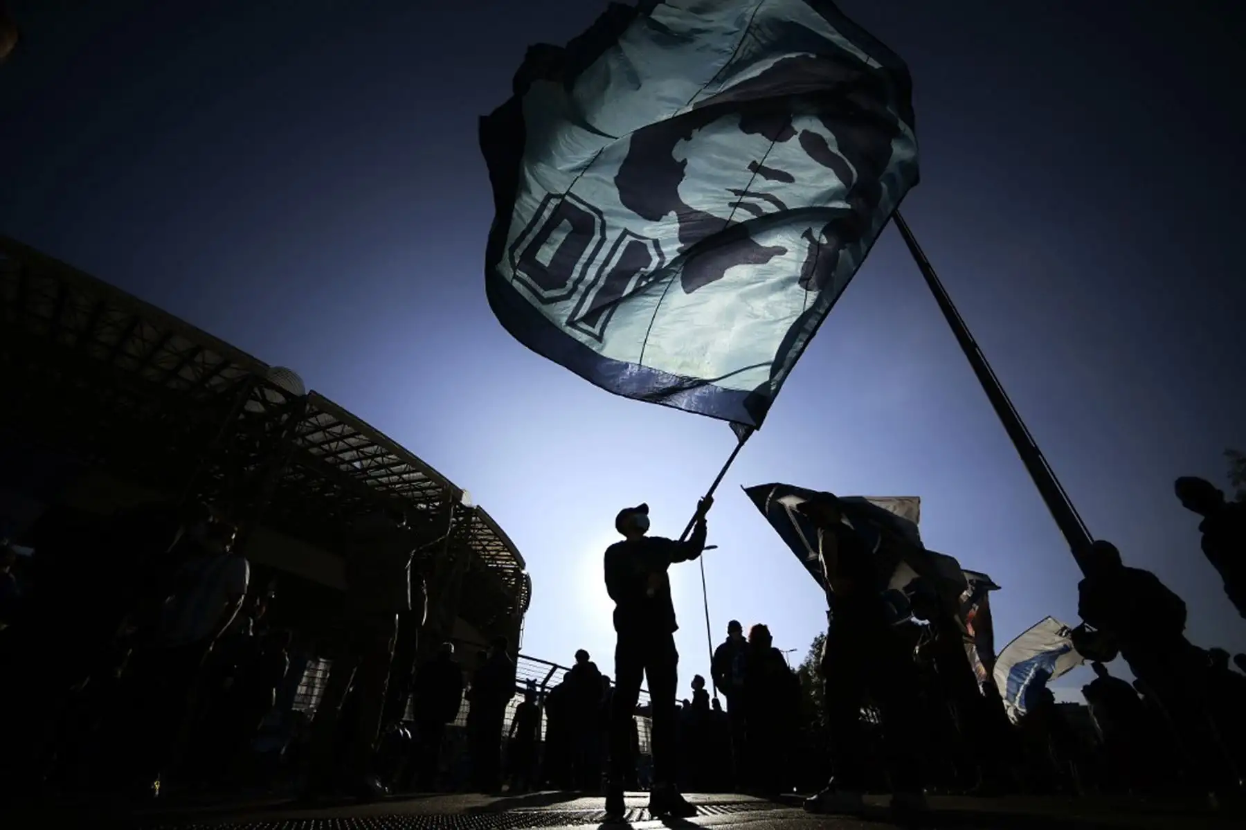 Un hombre agita una bandera ante la efigie de la leyenda del fútbol argentino Diego Maradona, mientras la gente se reúne el 26 de noviembre de 2020 frente al estadio San Paolo en Nápoles para llorar la muerte de su ídolo. Foto: AFP