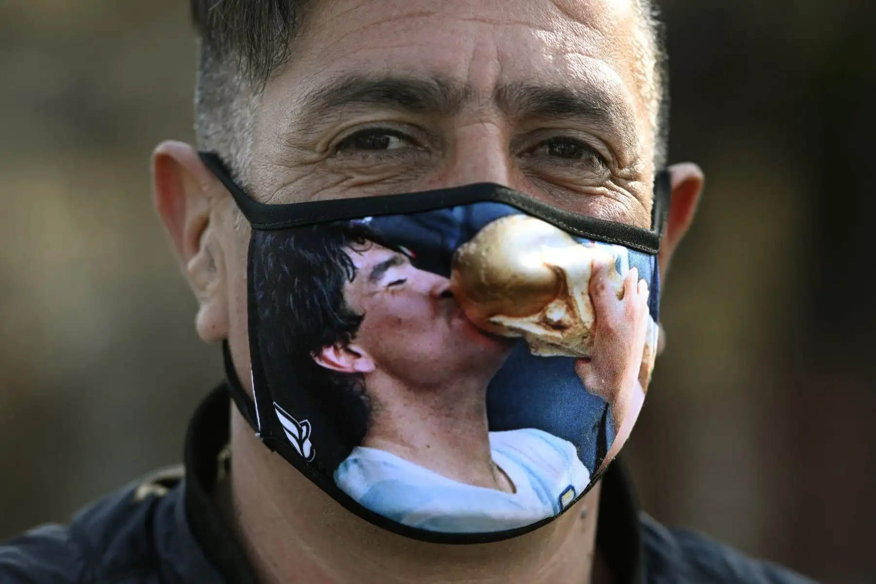 Un hombre posa con una máscara con el retrato del exfutbolista argentino Diego Maradona besando el trofeo de la Copa Mundial de la FIFA México 
