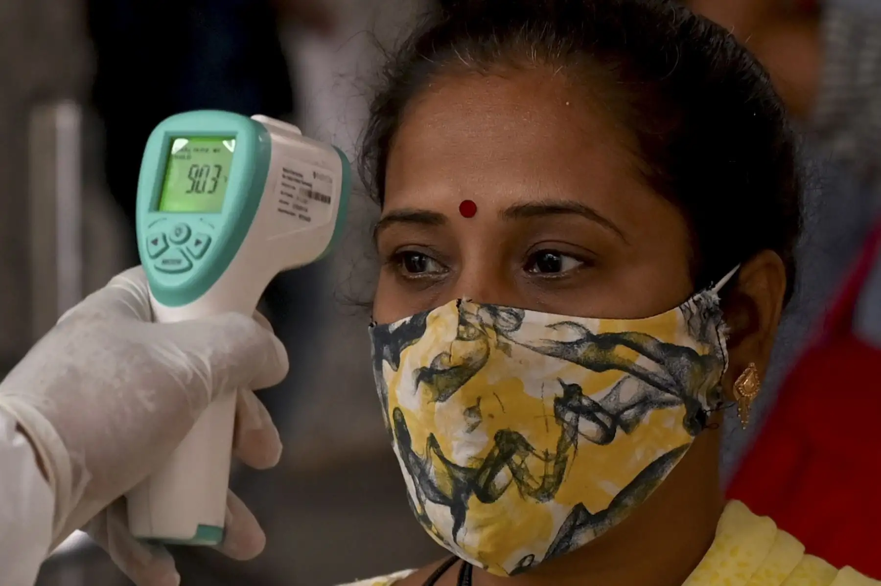 Un trabajador de la salud controla la temperatura corporal de un pasajero que llega, ya que tiene el mandato de someterse a una prueba de detección del coronavirus Covid-19 en una terminal ferroviaria en Mumbai. Foto: AFP