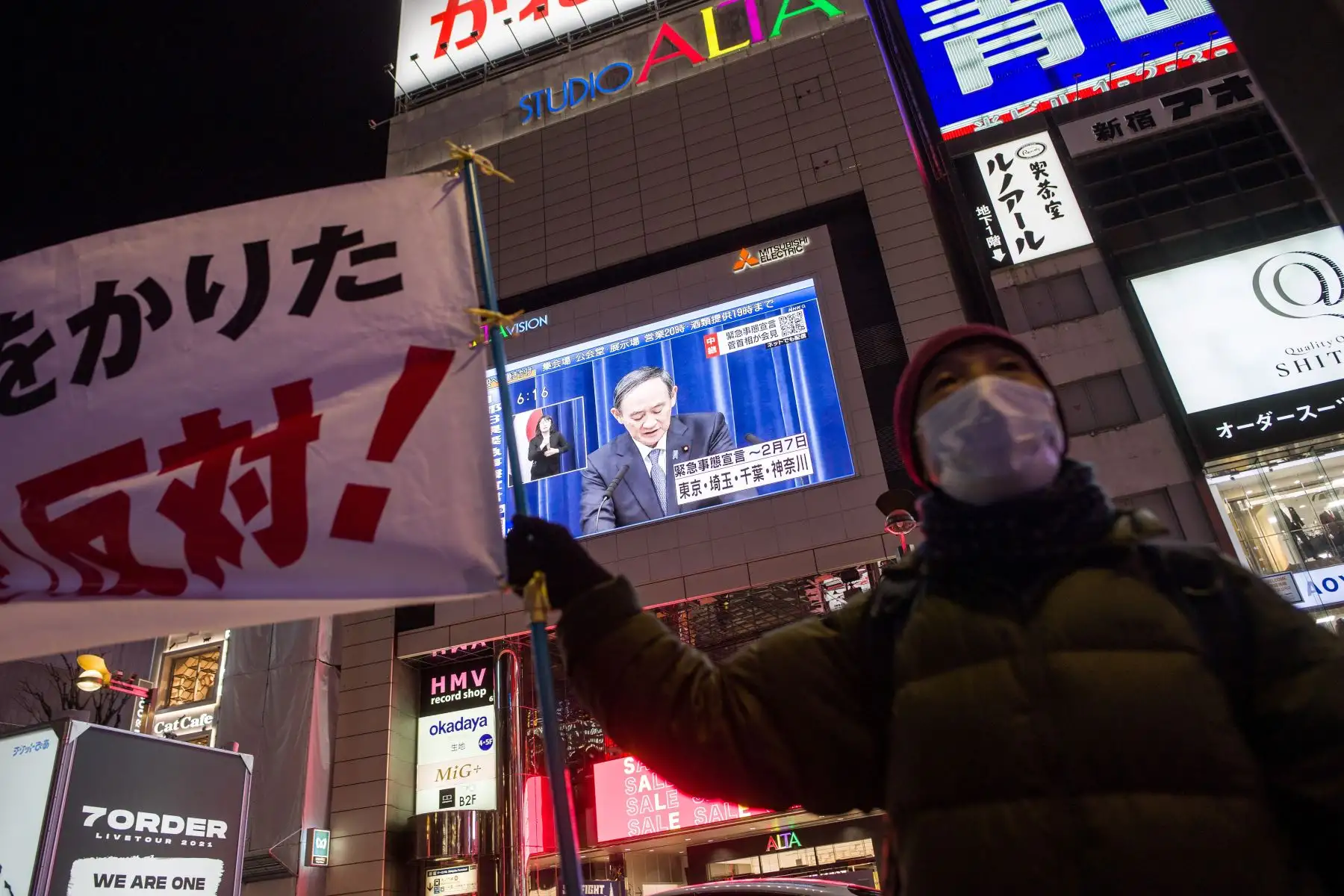 Un manifestante contra el estado de emergencia corea consignas mientras una pantalla grande, muestra al primer ministro japonés Yoshihide Suga durante una transmisión en vivo de una conferencia de prensa sobre un estado de emergencia declarado para el área metropolitana de Tokio. Foto:AFP