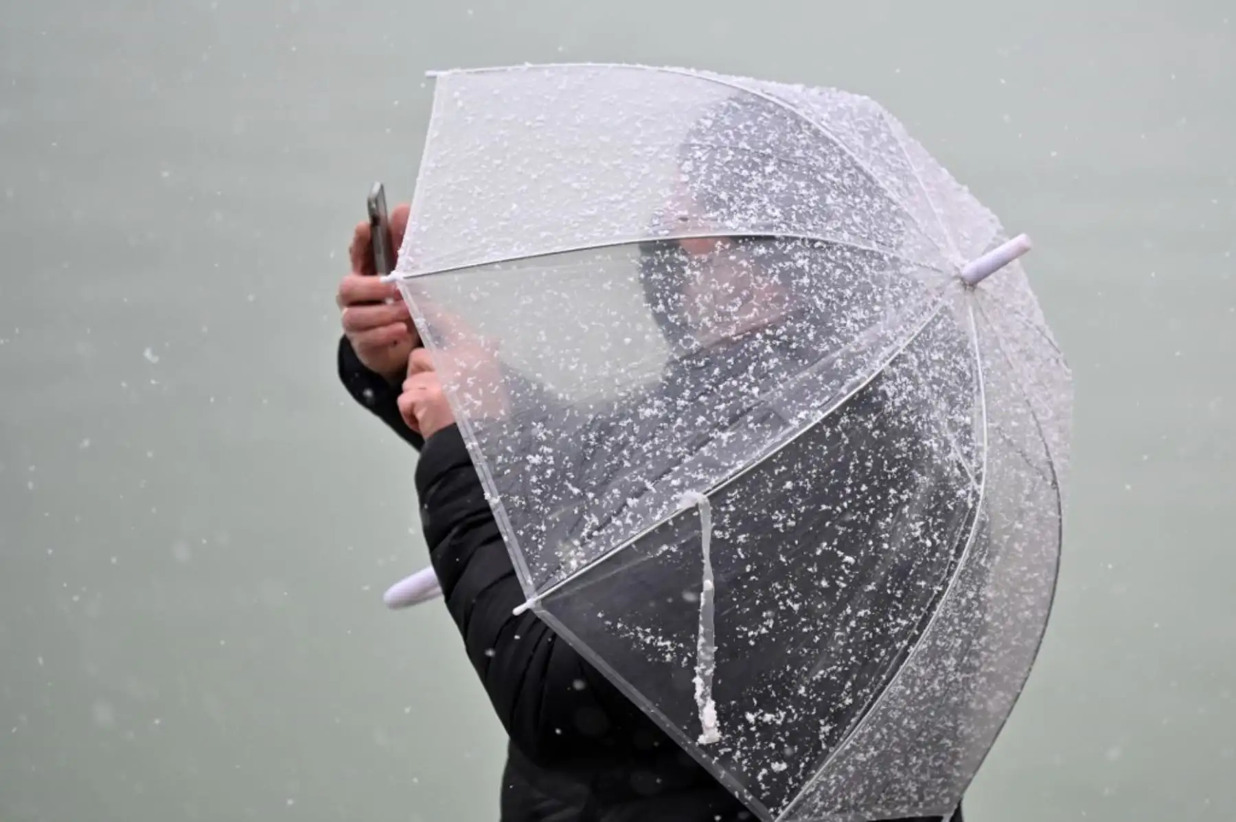 Un hombre saca una foto con su smartphone mientras cae la nieve en el Parque del Retiro en el centro de Madrid. Foto: AFP