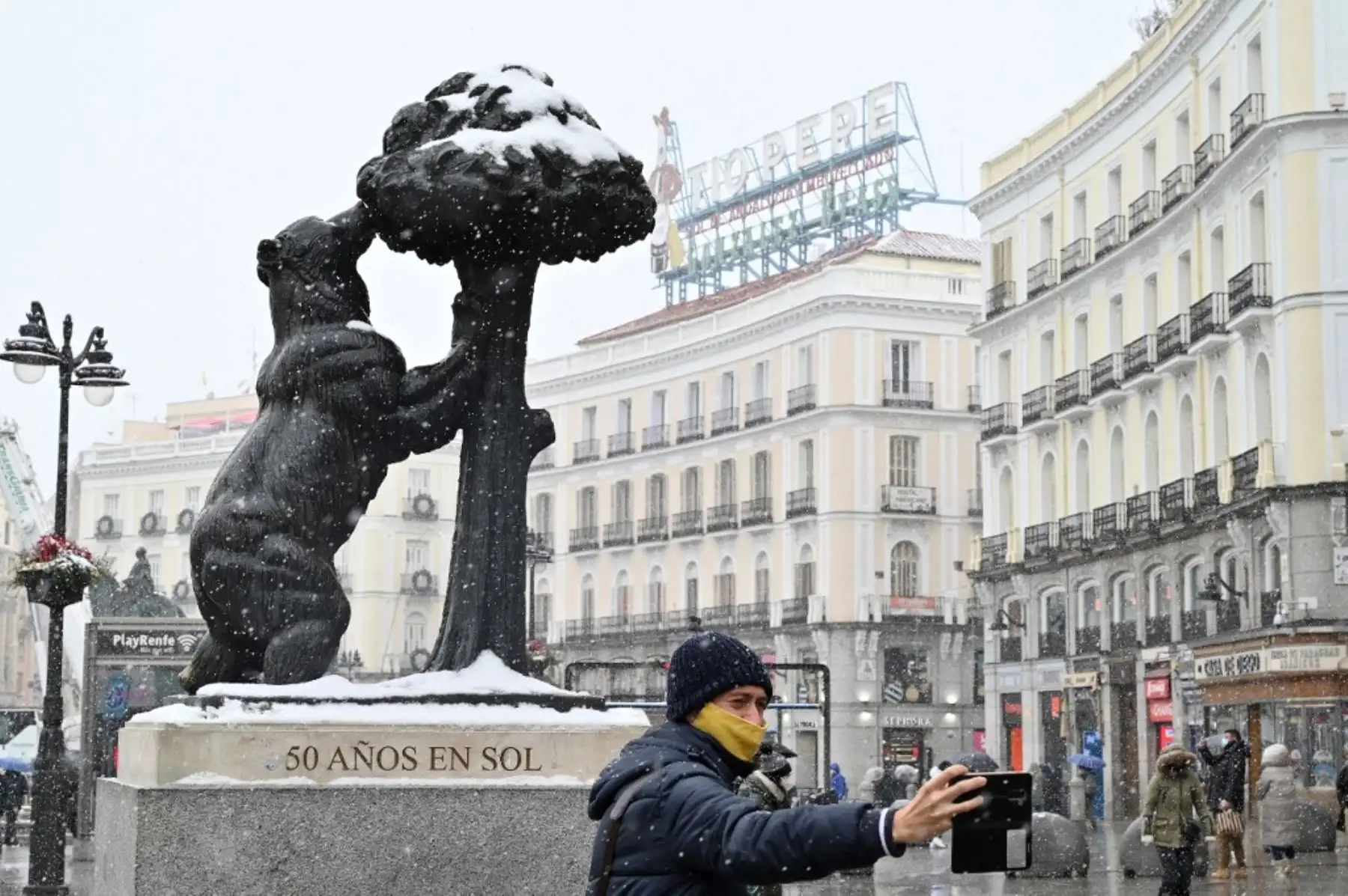 Un hombre se toma una foto junto a la estatua de "El Oso y El Madrono" (el oso y el madroño) en la plaza Puerta del Sol de Madrid el 8 de enero de 2021 durante una nevada. Foto: AFP