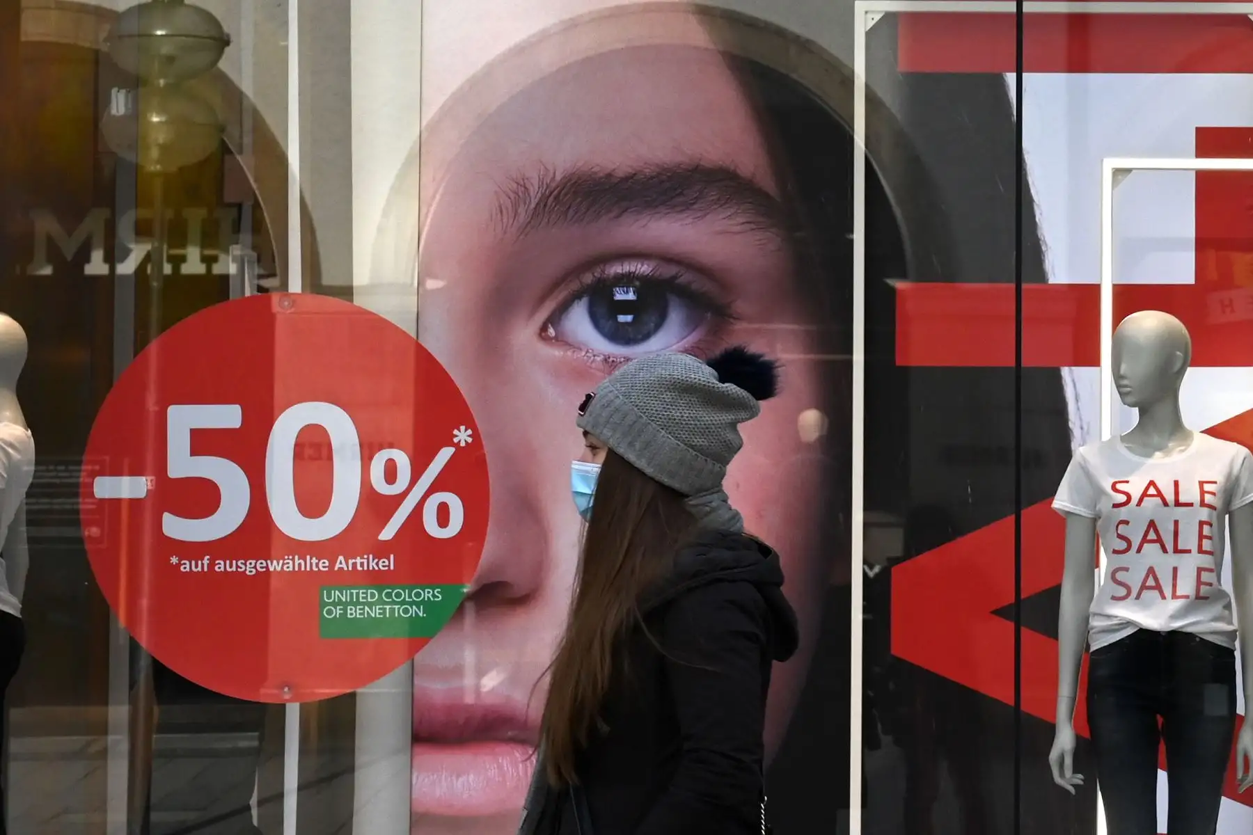 Una mujer con una máscara facial camina frente a una tienda de moda cerrada con ventas anunciadas en sus escaparates, en la ciudad de Múnich, en el sur de Alemania, en medio de la pandemia del nuevo coronavirus Covid-19 en curso. Foto: AFP
