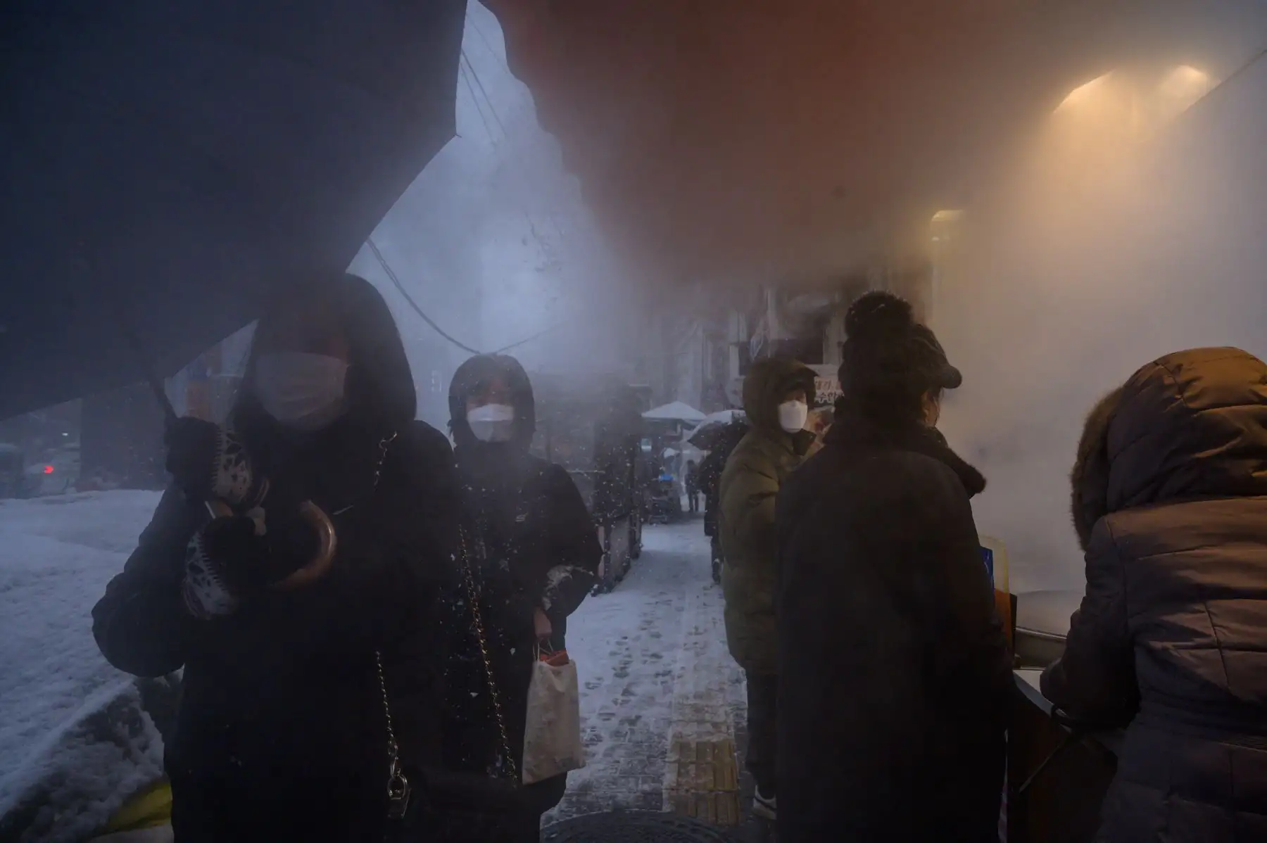 Los clientes esperan en la entrada de un mercado callejero durante una nevada en Seúl. Foto: AFP