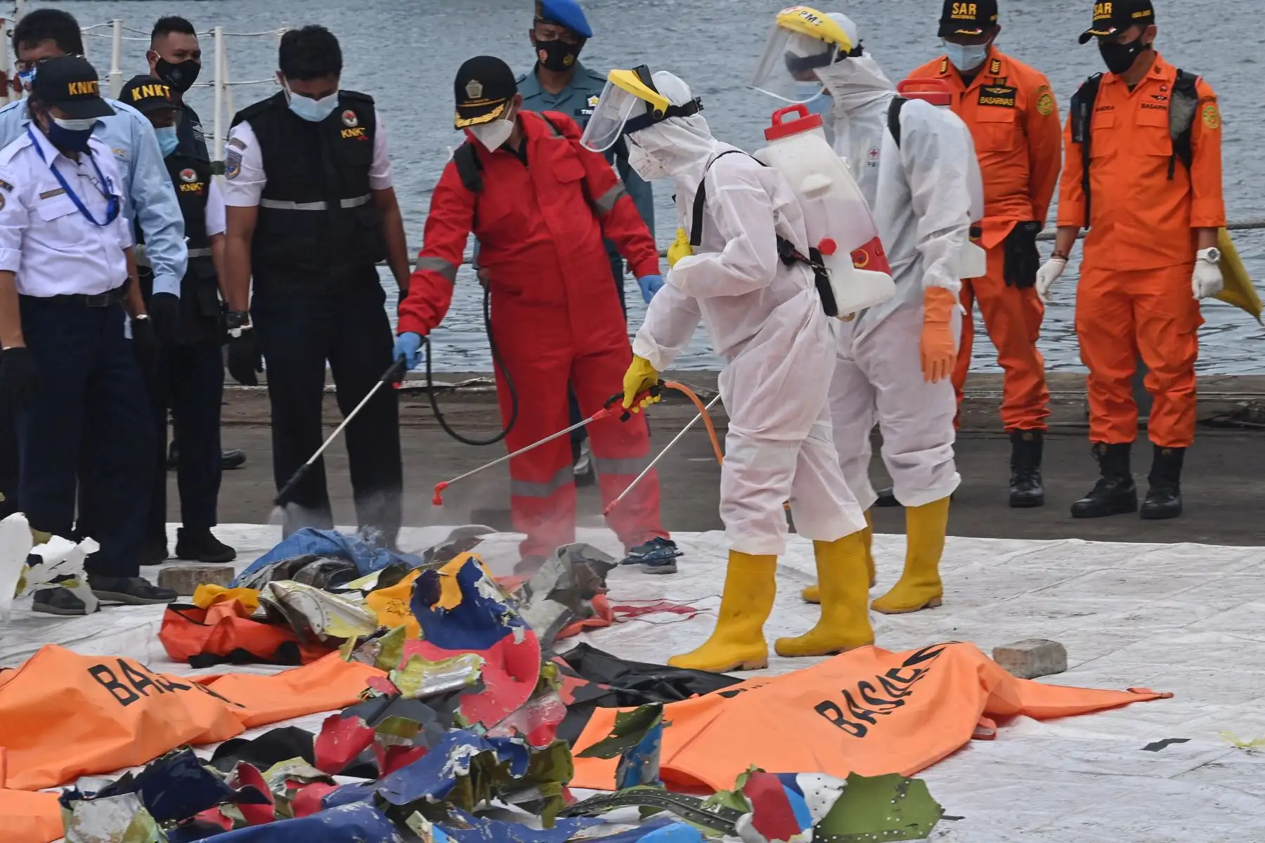 Miembros de la Cruz Roja Indonesia rocían desinfectante sobre artículos recuperados del vuelo SJ182 de Sriwijaya Air en el puerto de Tanjung Priok. Foto: AFP