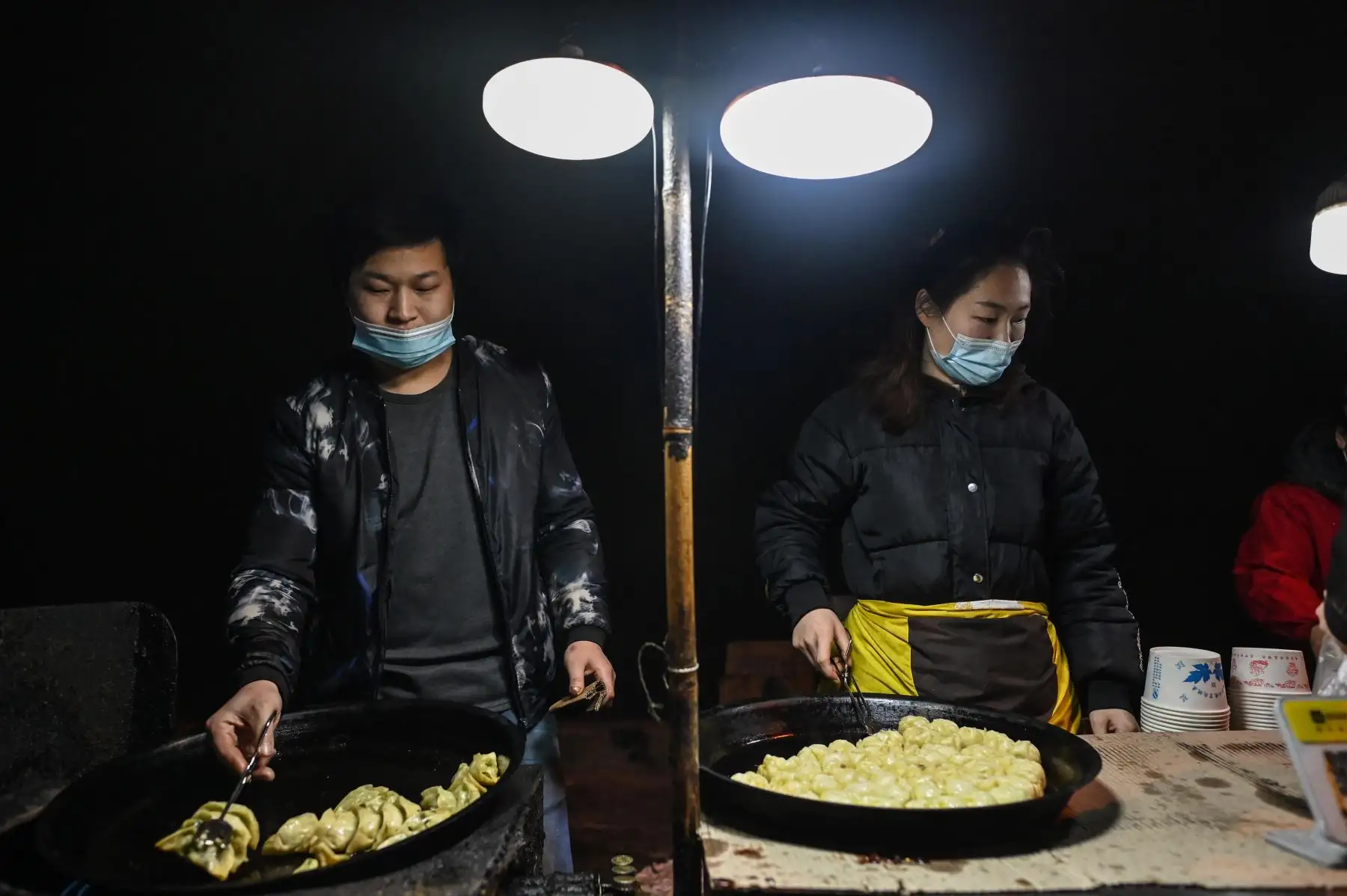 Una pareja que usa mascarilla como medida preventiva contra el covid-19, prepara comida para vender en una calle de Wuhan provincia de Hubei; en el centro de China.
Foto: AFP