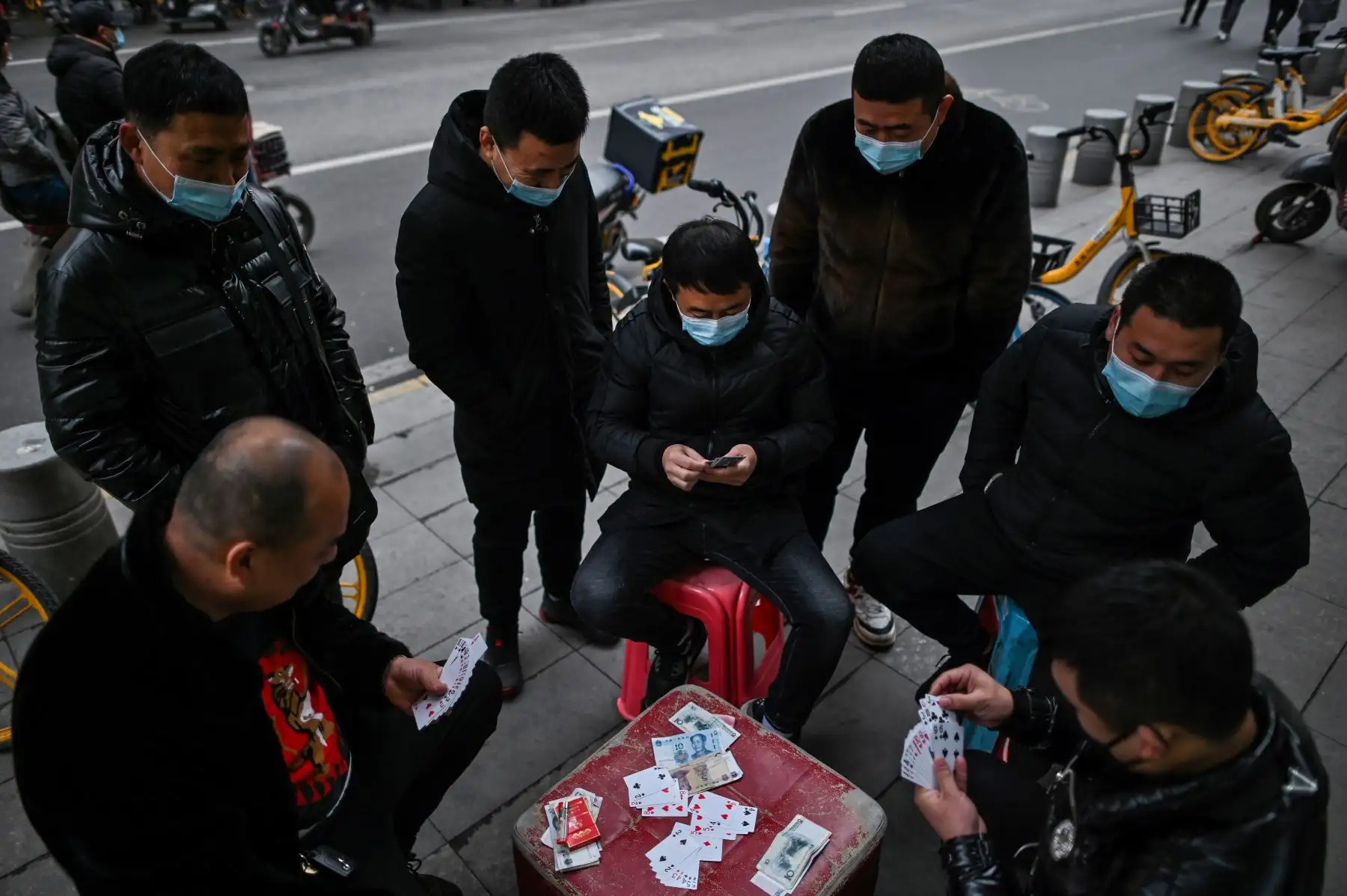 Hombres con mascarillas como medida preventiva contra el coronavirus Covid-19 juegan a las cartas en una calle de Wuhan. Foto: AFP