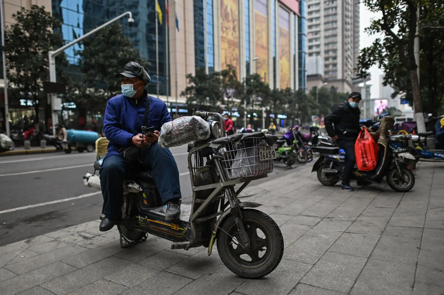 Un hombre que llevaba una mascarilla como medida preventiva contra el coronavirus Covid-19 descansa sobre su scooter en Wuhan. Foto: AFP