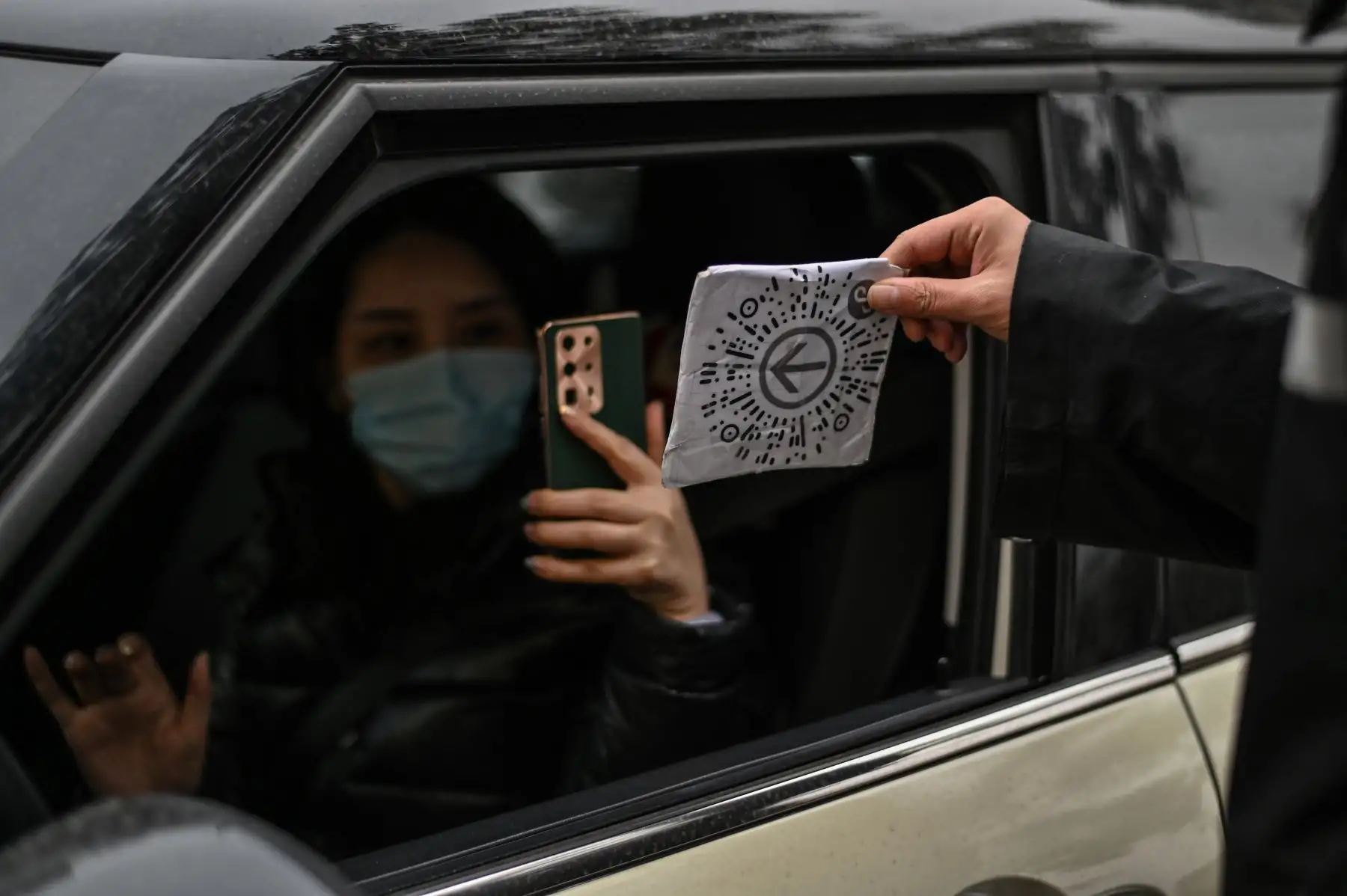Una mujer con mascarilla como medida preventiva contra el coronavirus Covid-19 escanea un código de salud para ingresar al área de estacionamiento de un centro comercial en Wuhan. Foto: AFP