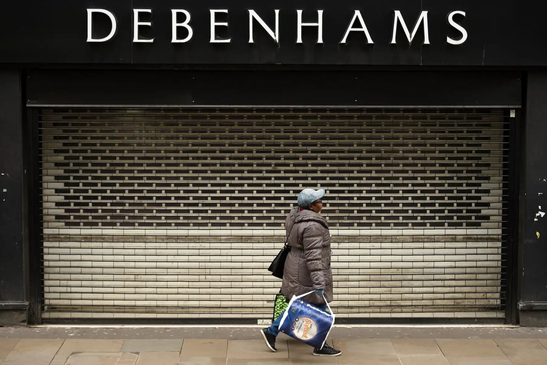 Una mujer pasa frente a las contraventanas en la entrada de los grandes almacenes Debenhams en Manchester, en el noroeste de Inglaterra. Foto: AFP