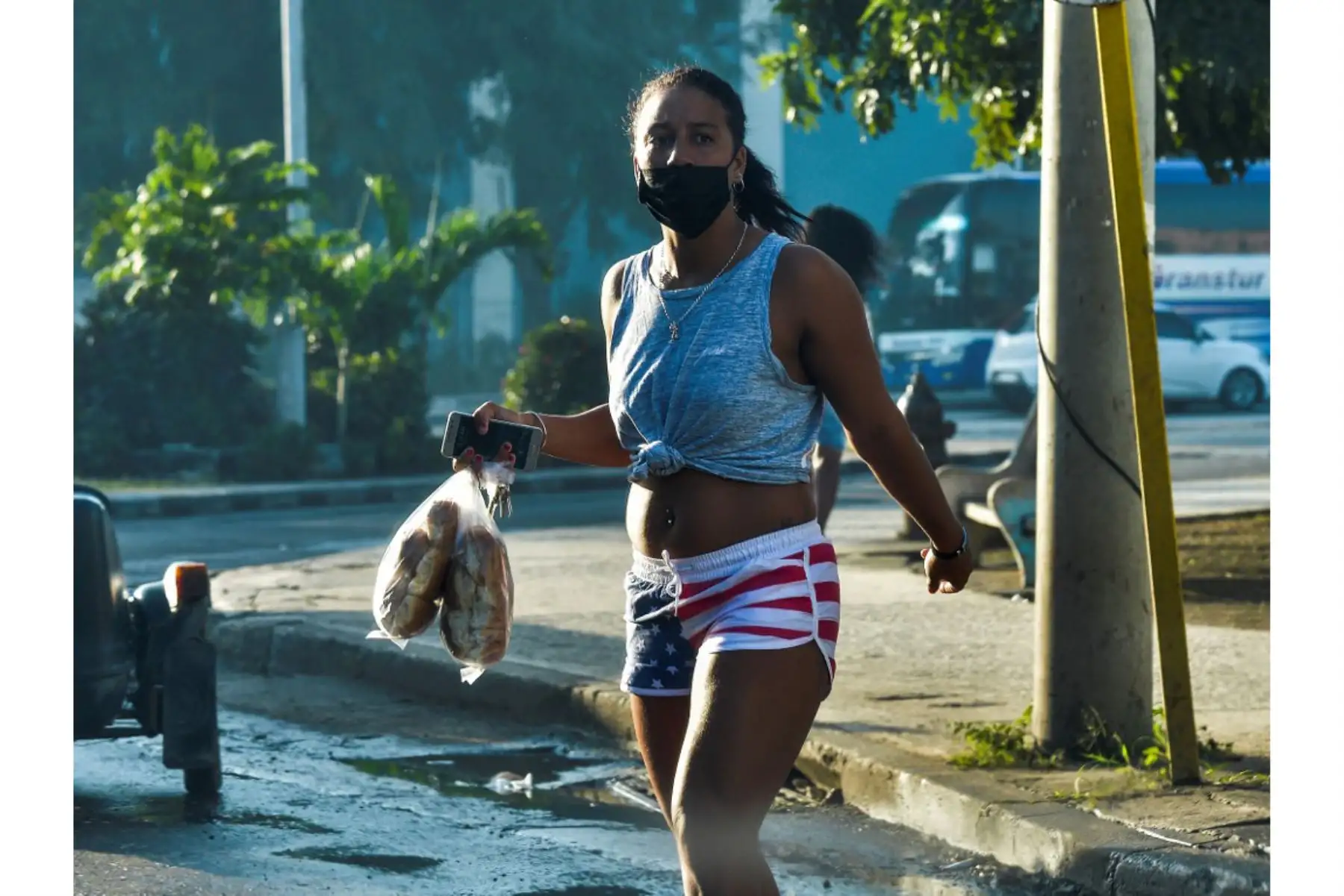 Una mujer con mascarilla y un pantalón corto con la bandera de Estados Unidos carga bolsas de pan mientras camina por una calle de La Habana. Investigadores cubanos se han centrado en la tarea de desarrollar la primera vacuna contra covid-19 concebida y producido en América Latina. Foto: AFP