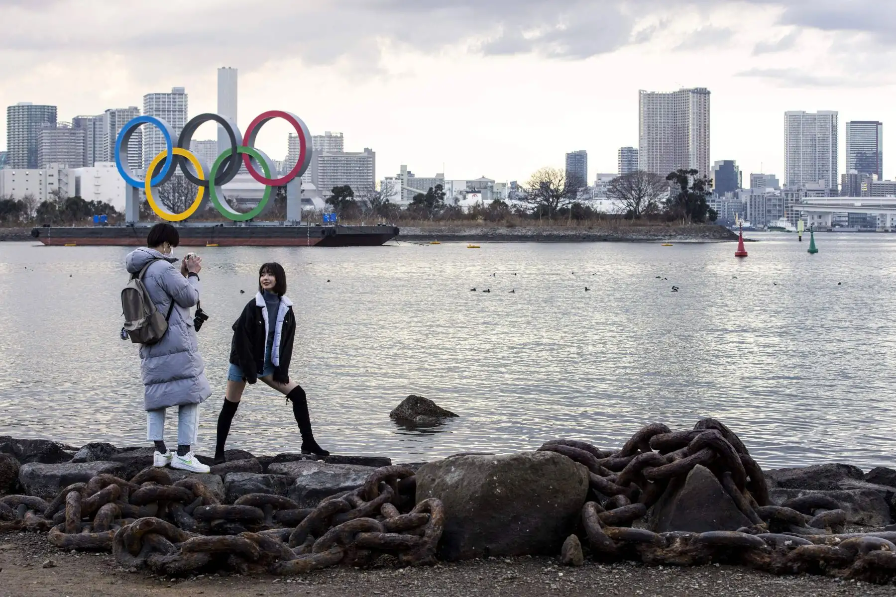 Una mujer posa para fotografías frente a los anillos olímpicos que se exhiben en el paseo marítimo de Odaiba en Tokio. El gobierno de Japón aprobó extensión de un mes de su estado de emergencia por coronavirus.