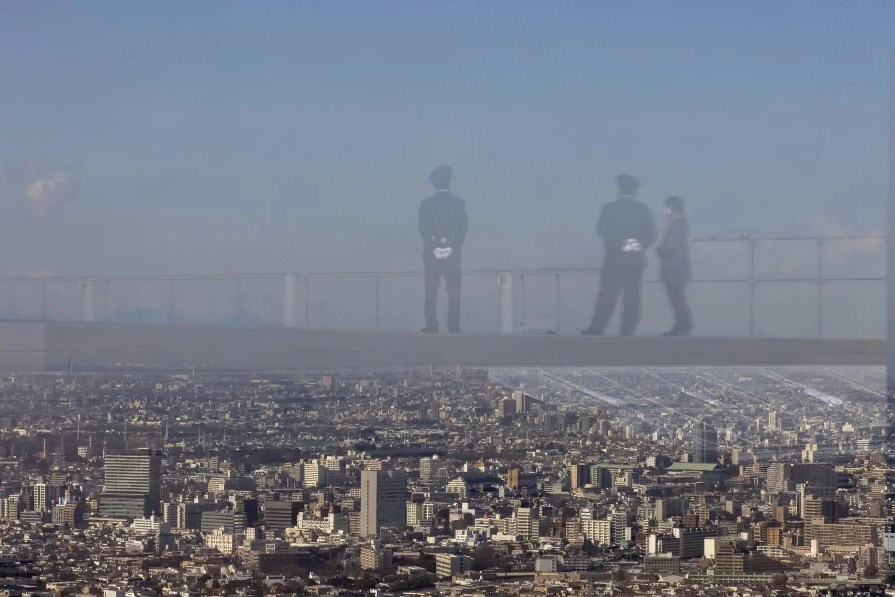 Los guardias de seguridad se reflejan en una barrera de vidrio en la plataforma de observación Shibuya Sky en Tokio. El gobierno de Japón aprobó extensión de un mes de su estado de emergencia por coronavirus. Foto: AFP