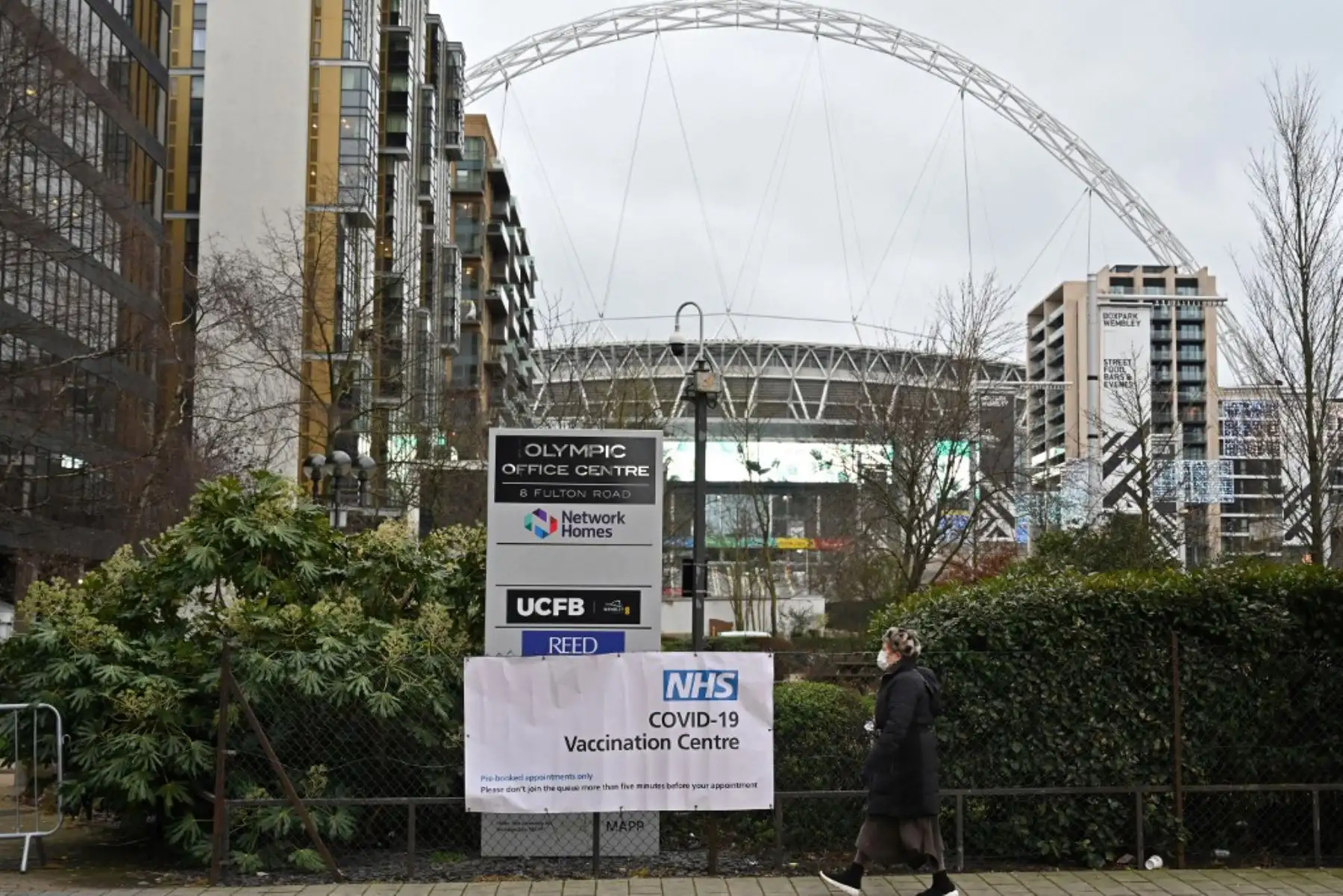 Un peatón que cubre la cara pasa junto a un cartel de un centro de vacunación NHS covid-19 en Wembley, noroeste de Londres. Foto: AFP