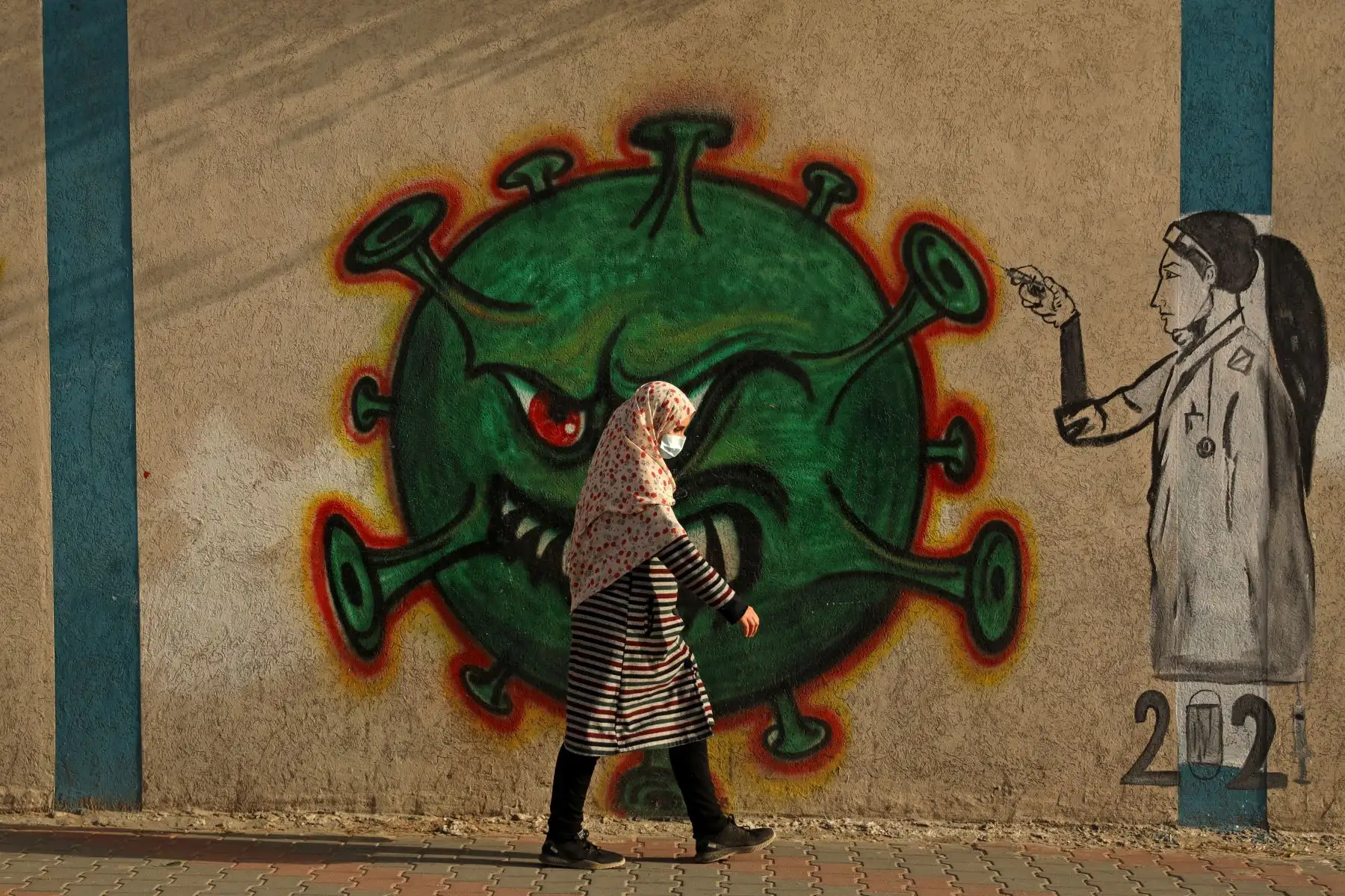 Una mujer palestina, con una máscara protectora en medio de la pandemia de covid-19, pasa frente a un mural inspirado en el coronavirus en la ciudad de Gaza.

Foto: AFP