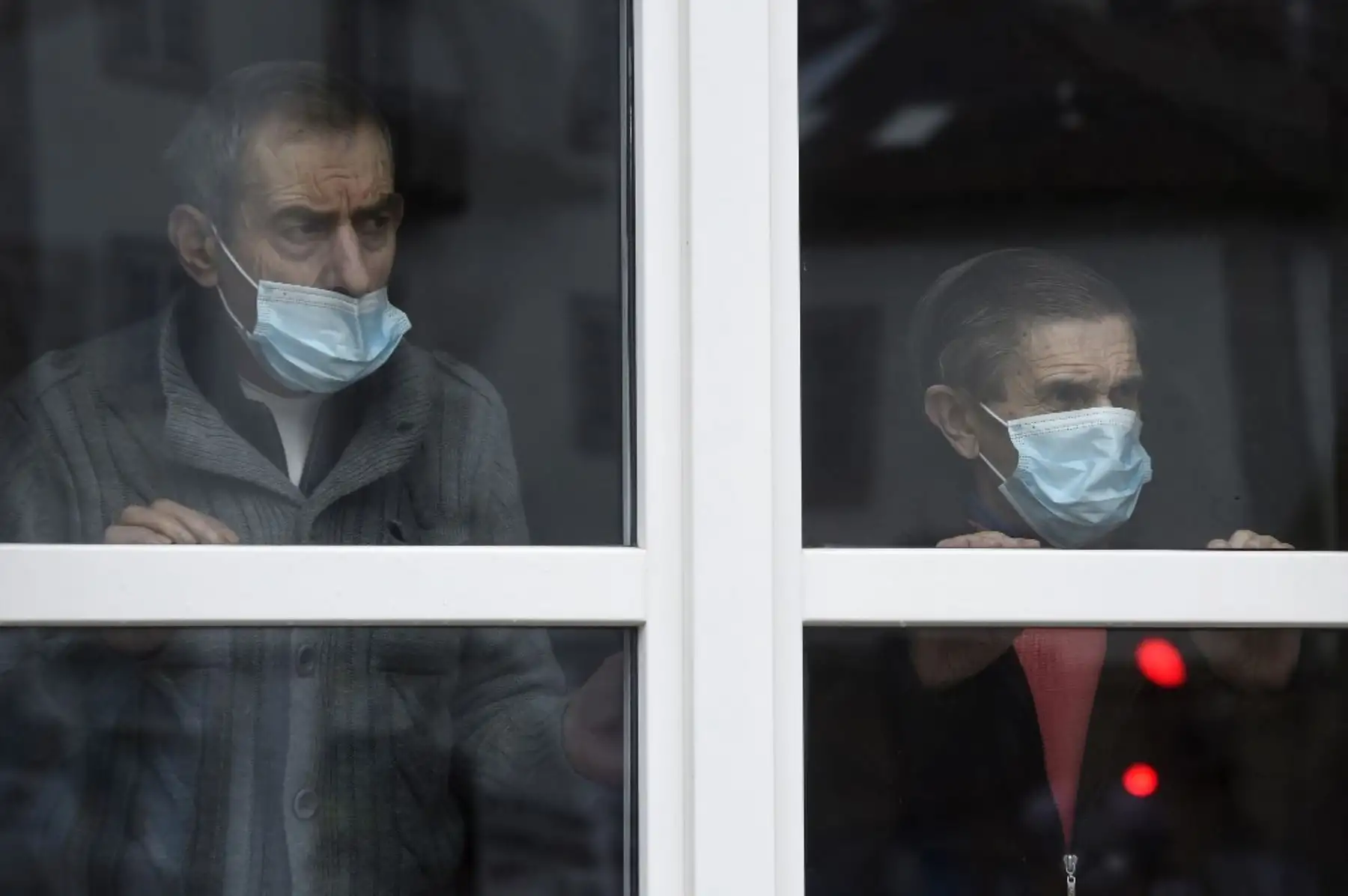 Dos ancianos con mascarillas miran por la ventana de la residencia Porta do Camino en Santiago de Compostela, noroeste de España. Foto: AFP