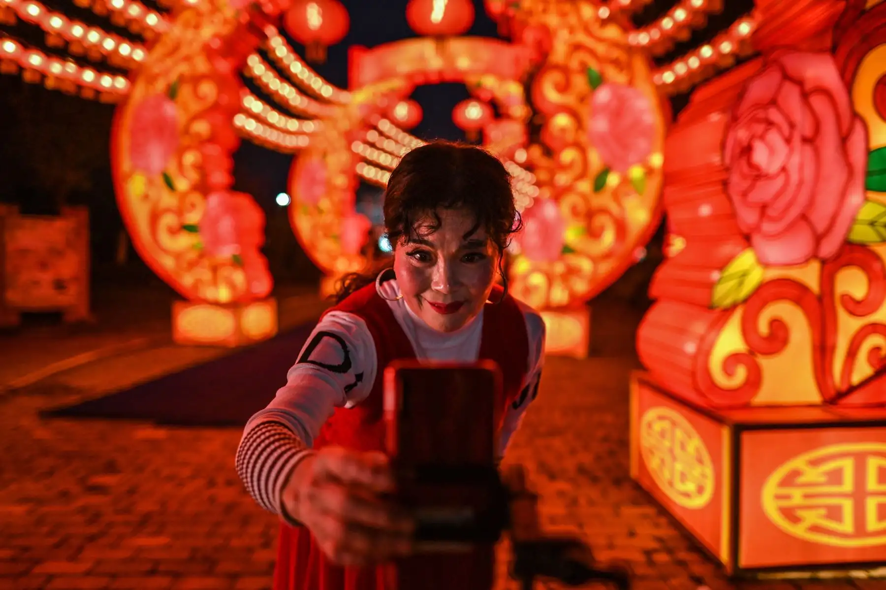 Una mujer revisa su teléfono móvil después de grabar un video de ella bailando junto a linternas en un parque en Wuhan en la provincia central china de Hubei el 11 de febrero de 2021, antes del inicio del Año Nuevo Lunar, que marca el comienzo del Año del Buey. Foto: AFP