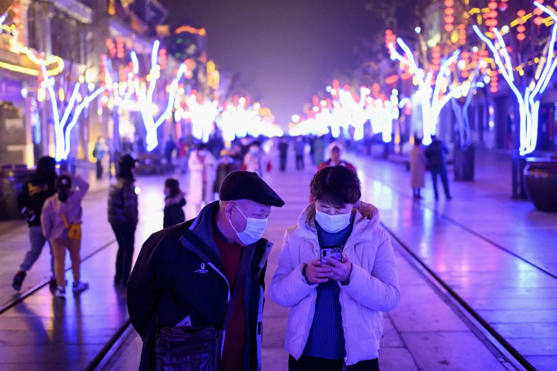 Personas con máscaras miran su teléfono móvil en la calle Qianmen en Beijing el 11 de febrero de 2021, antes del Año Nuevo Lunar. Foto: AFP