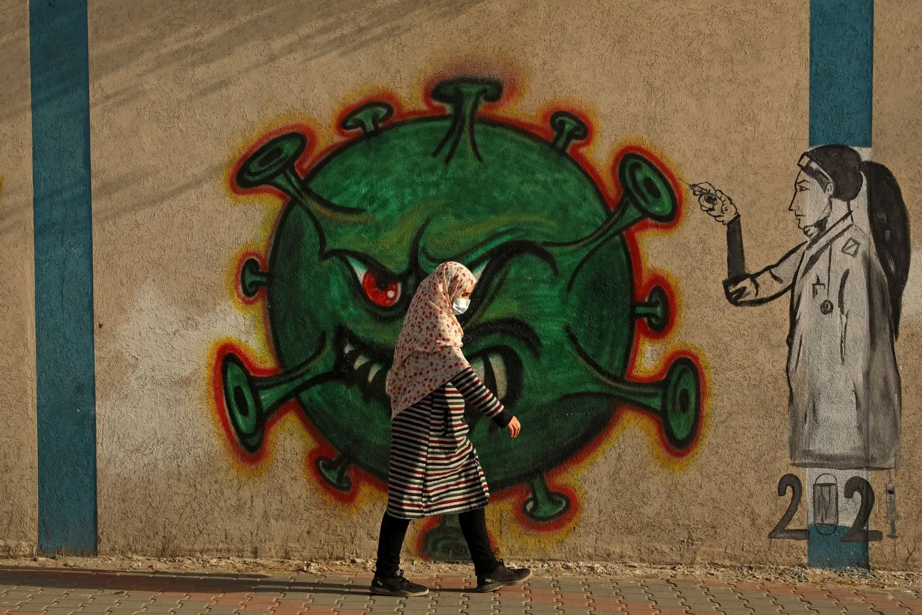 Una mujer palestina, con una máscara protectora en medio de la pandemia de COVID-19, pasa frente a un mural inspirado en el coronavirus en la ciudad de Gaza, el 2 de febrero de 2021. Foto: AFP