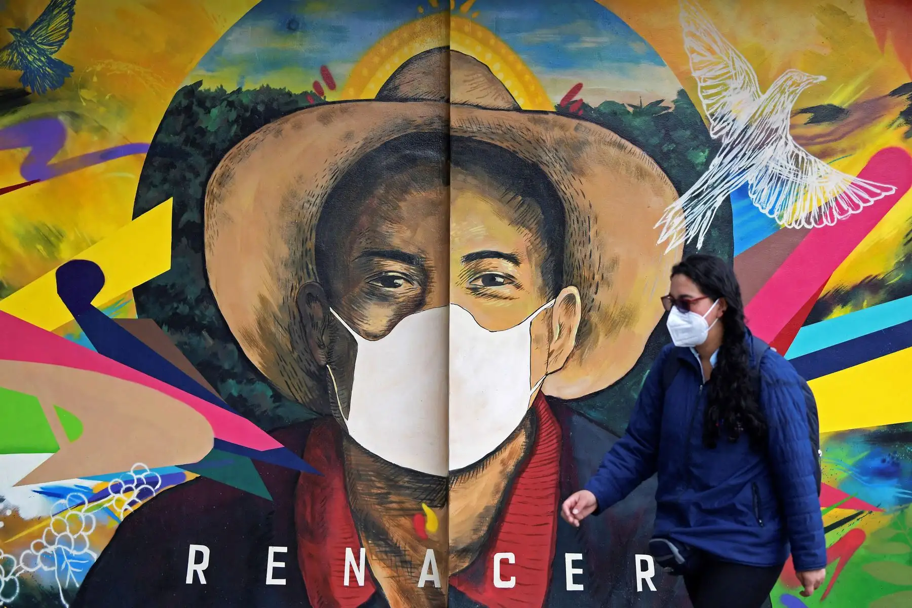 Una mujer con máscara facial camina junto a una pared pintada en Bogotá, Colombia, el 10 de febrero del 2021. Foto: AFP