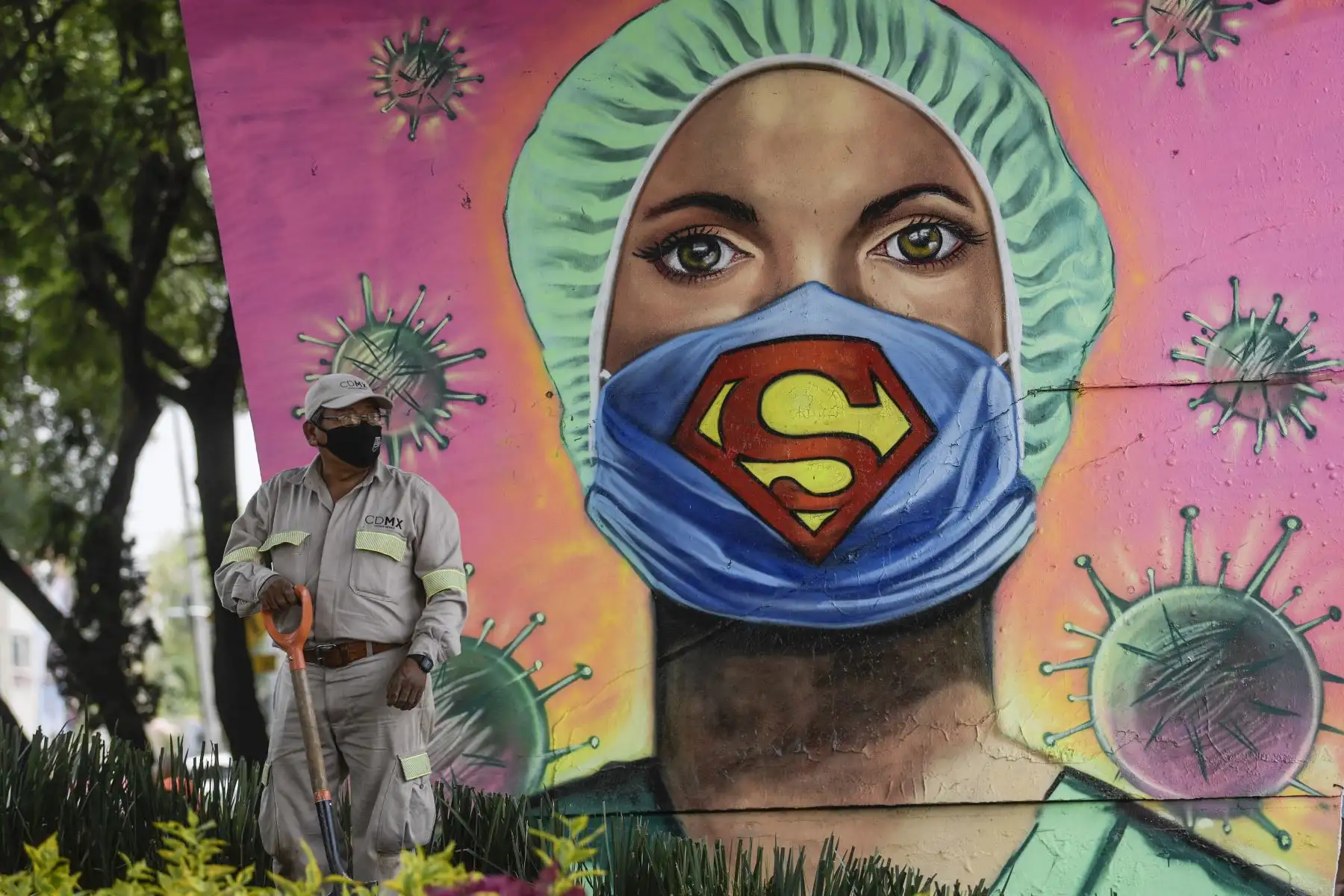 Un jardinero de la ciudad trabaja junto a un mural que muestra a un trabajador de la salud con una mascarilla con el símbolo del superhéroe ficticio Superman, firmado por el artista urbano Applez, en la Ciudad de México, el 21 de julio de 2020. Foto: AFP