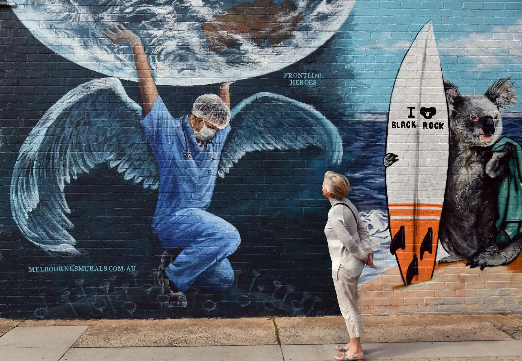 Una mujer mira un mural de un trabajador de la salud con alas sosteniendo un globo terráqueo en el Día Internacional de la Enfermera en Melbourne el 12 de mayo de 2020. Foto: AFP