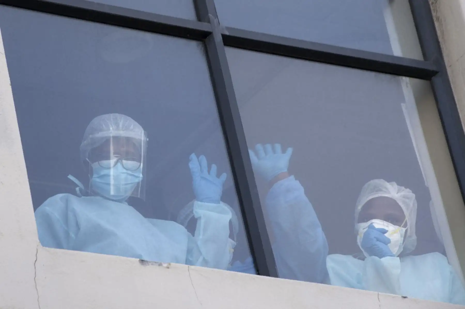 Los miembros del personal de la sala covid-19 en el Centro Médico Rondebosch saludan a las personas reunidas fuera del edificio mientras participan en una reunión interreligiosa para orar por los pacientes covid-19 y sus cuidadores en el Centro Médico Rondebosch, en Ciudad del Cabo. Foto: AFP
