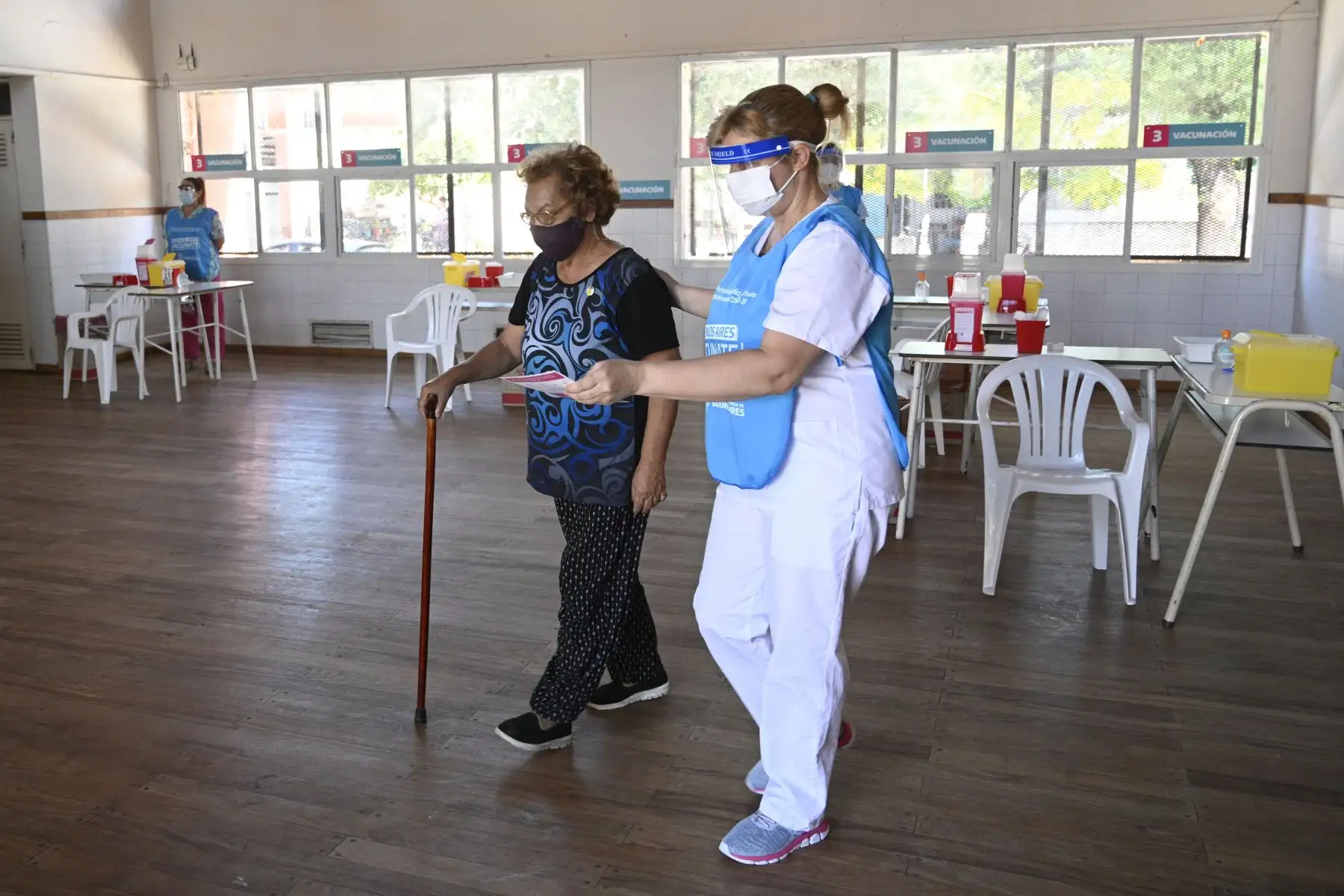 Una anciana camina acompañada por un trabajador de salud luego de recibir una dosis de la vacuna Sputnik V contra COVID-19, en un centro de vacunación temporal de una escuela pública en Ezeiza, afueras de Buenos Aires. Foto: AFP