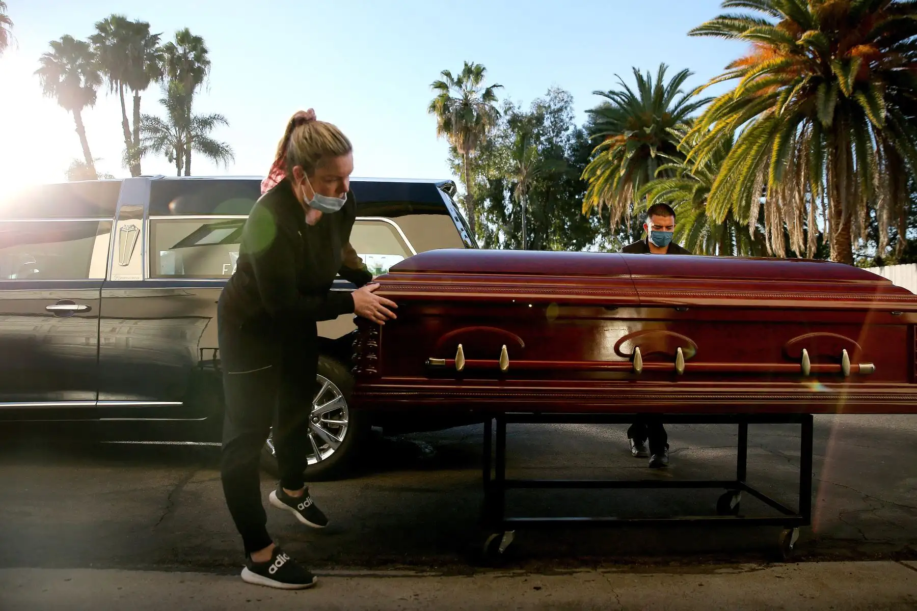 El embalsamador y director de la funeraria Kristy Oliver y el asistente de la funeraria Sam Deras se preparan para cargar el ataúd de una persona que murió después de contraer el COVID-19 en un coche fúnebre en East County Mortuary. Foto: AFP