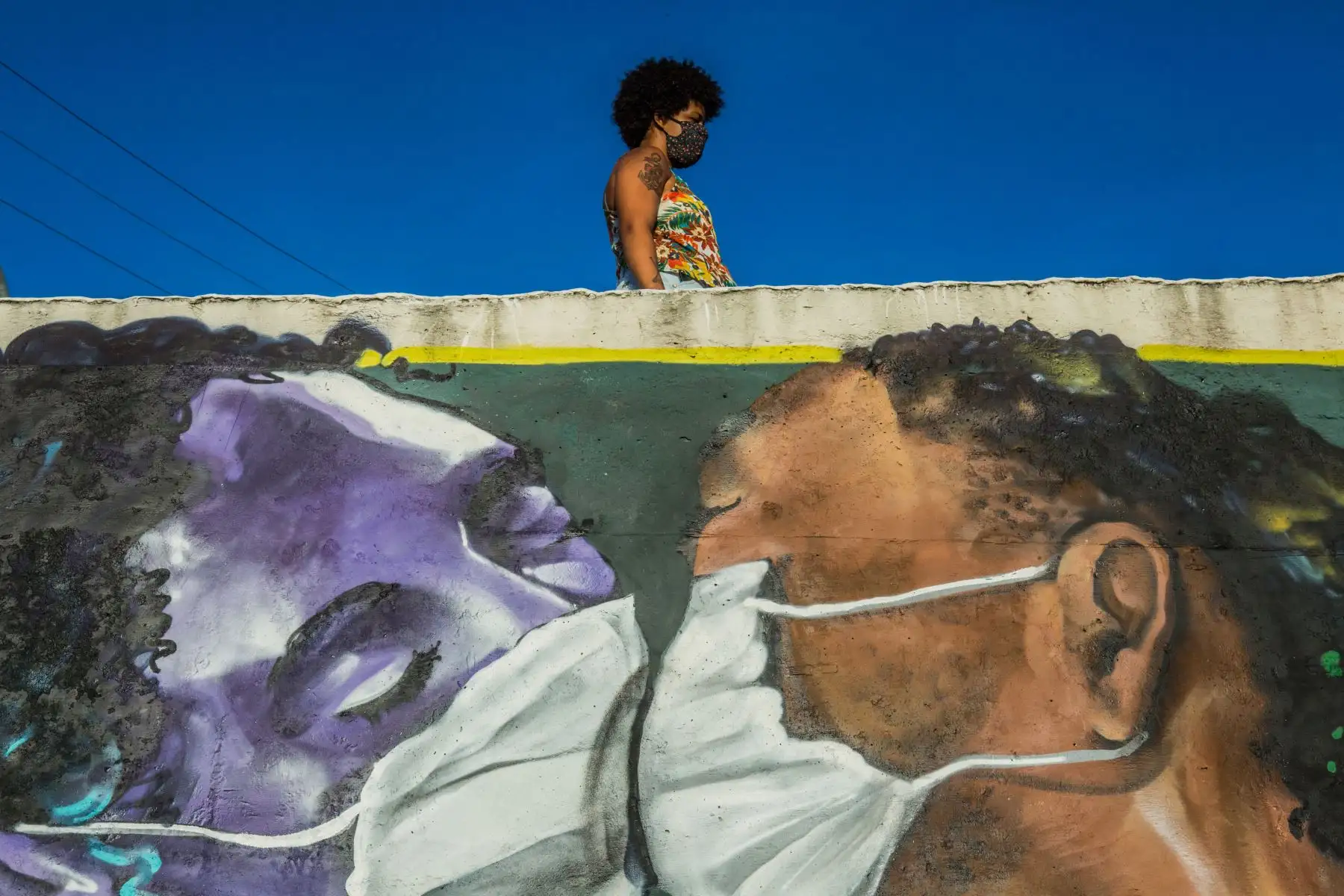 Una mujer con una máscara facial se encuentra sobre un graffiti del artista Marcos Costa, o Spray Cabuloso, en la entrada de la favela Solar de Unhao en Salvador, estado de Bahía, Brasil. Desde el comienzo de la epidemia más de 111.331.990 personas contrajeron la enfermedad. De ellas al menos 68.323.000 se recuperaron, según las autoridades. Foto: AFP