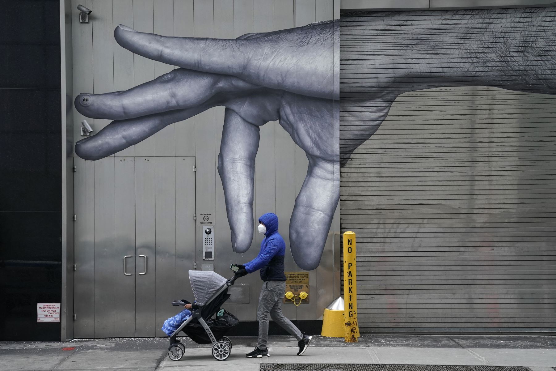 Una persona usa una mascarilla mientras empuja un cochecito de bebé frente a un mural de una mano en el muelle de carga en el Upper East Side de la ciudad de Nueva York. Foto: AFP