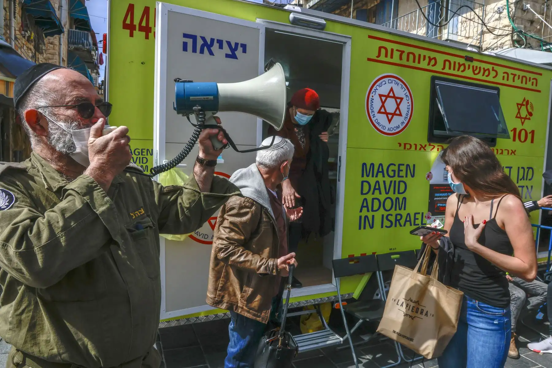 Un oficial del Home Front Command de Israel usa un megáfono para llamar a los pacientes durante una campaña de vacunación contra el coronavirus en el mercado Mahane Yehuda en Jerusalén el 22 de febrero de 2021. Foto: AFP