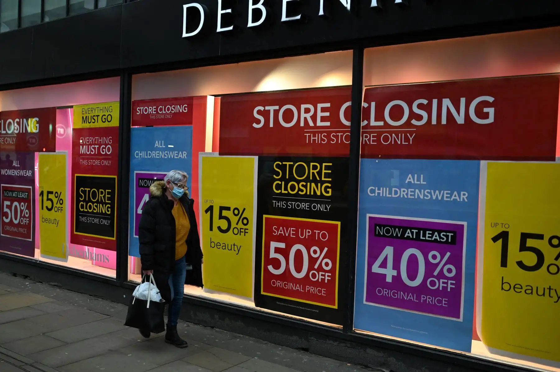 Un peatón pasa junto a los carteles de rebajas en las ventanas de Debenhams en el centro de la ciudad de Manchester el 19 de febrero de 2021, mientras la vida continúa bajo el tercer bloqueo británico. Foto: AFP