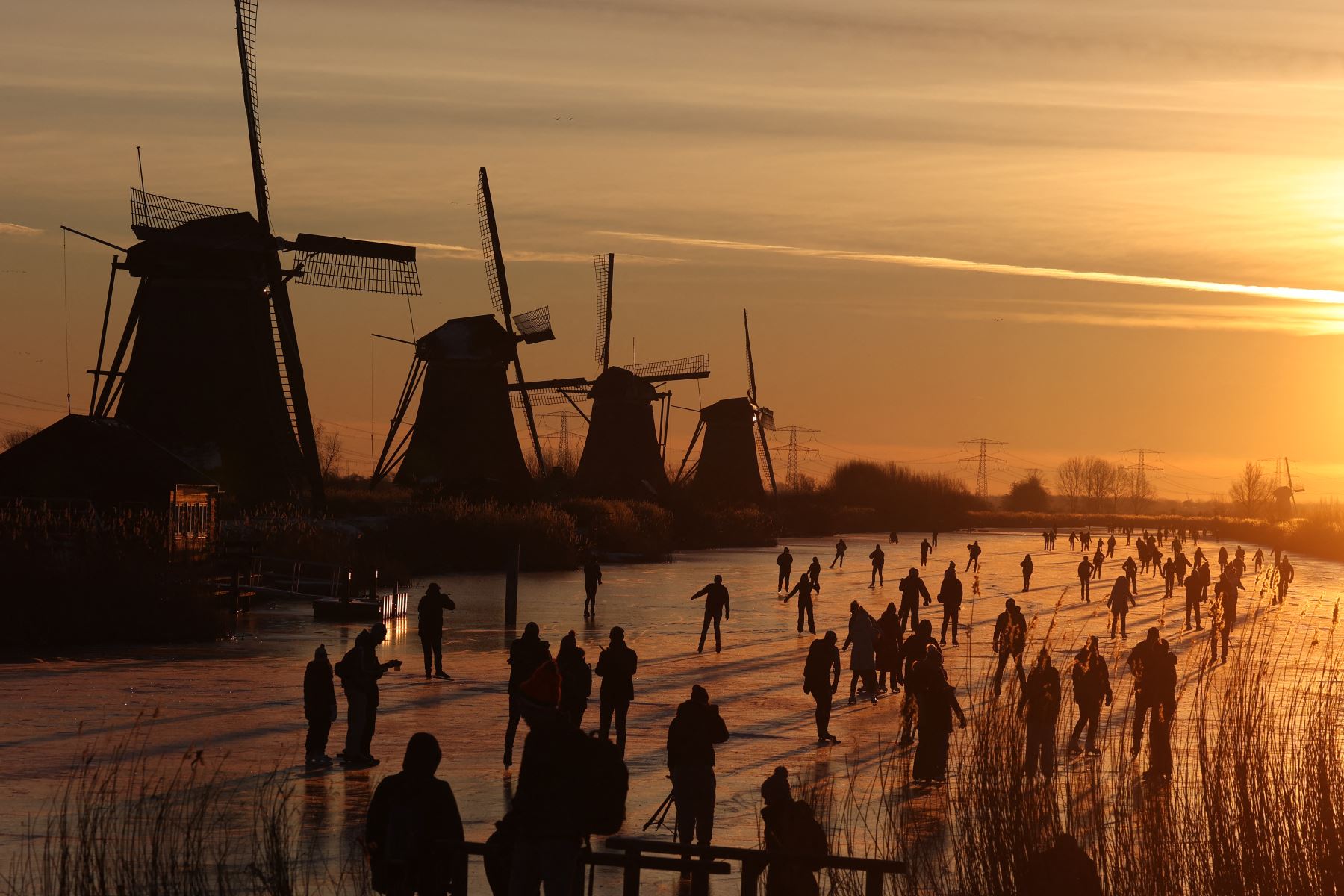 Los patinadores se deslizan sobre el hielo cerca de los molinos de viento en el pueblo de Kinderdijk, en Holanda. Foto: AFP
