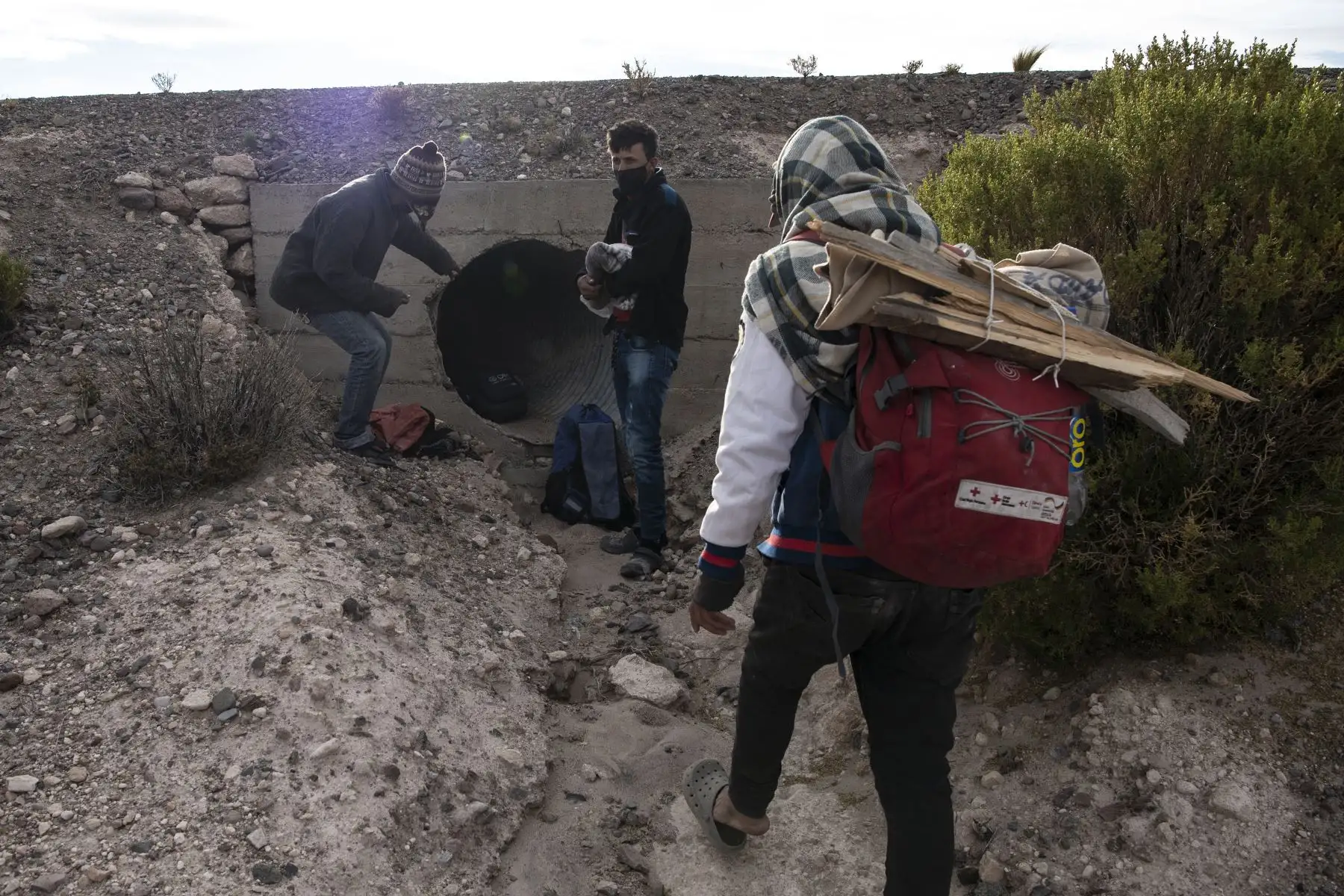 El migrante venezolano Rubi Alexander G. y sus amigos buscan refugio en un drenaje de agua de lluvia para pernoctar en la Ruta 15, cerca de Quebe, Chile luego de cruzar desde Bolivia. Foto: AFP