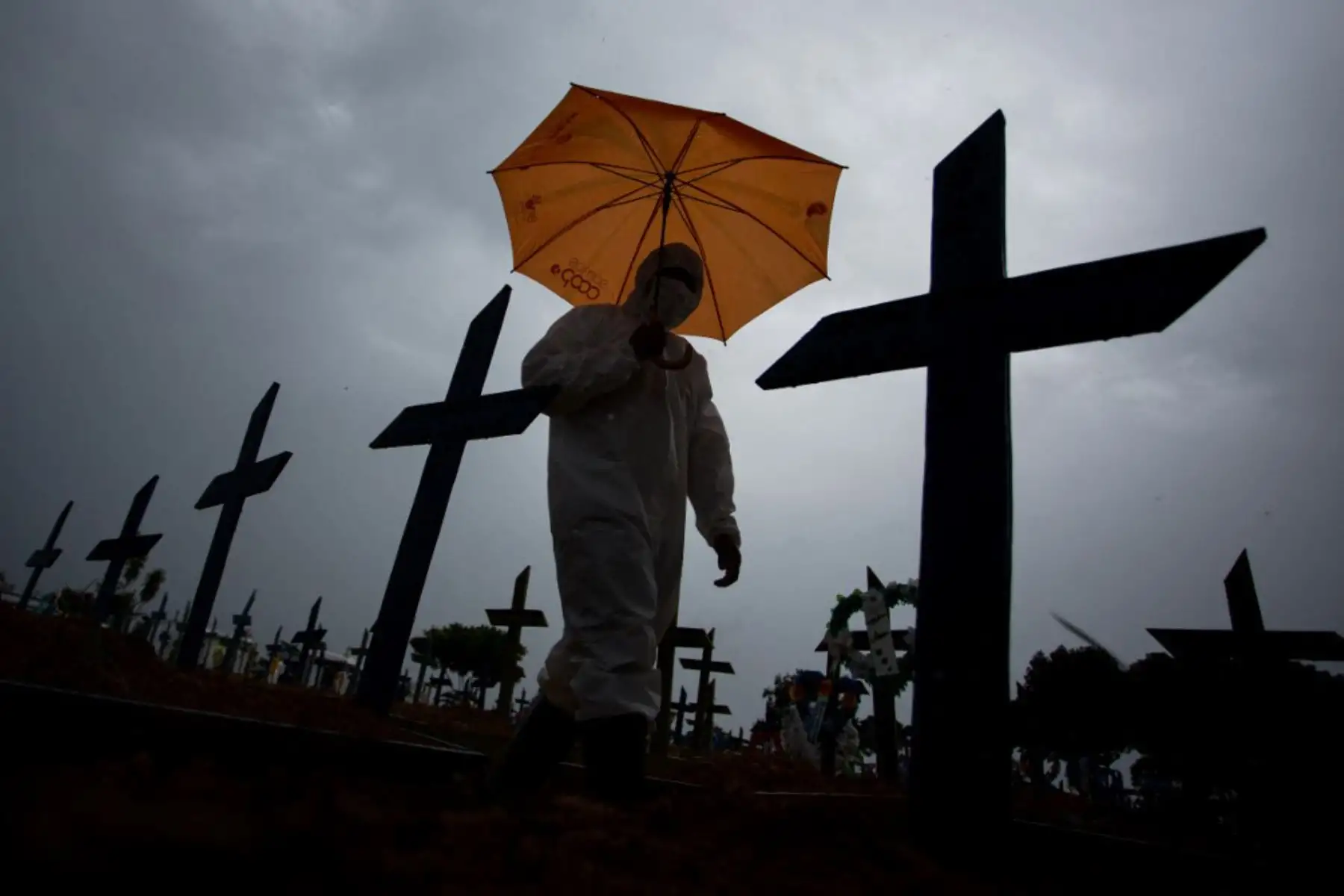 Un trabajador vestido con un traje protector y portando un paraguas pasa junto a las tumbas de las víctimas del covid-19 en el cementerio Nossa Senhora Aparecida, en Manaus, Brasil. Foto: AFP