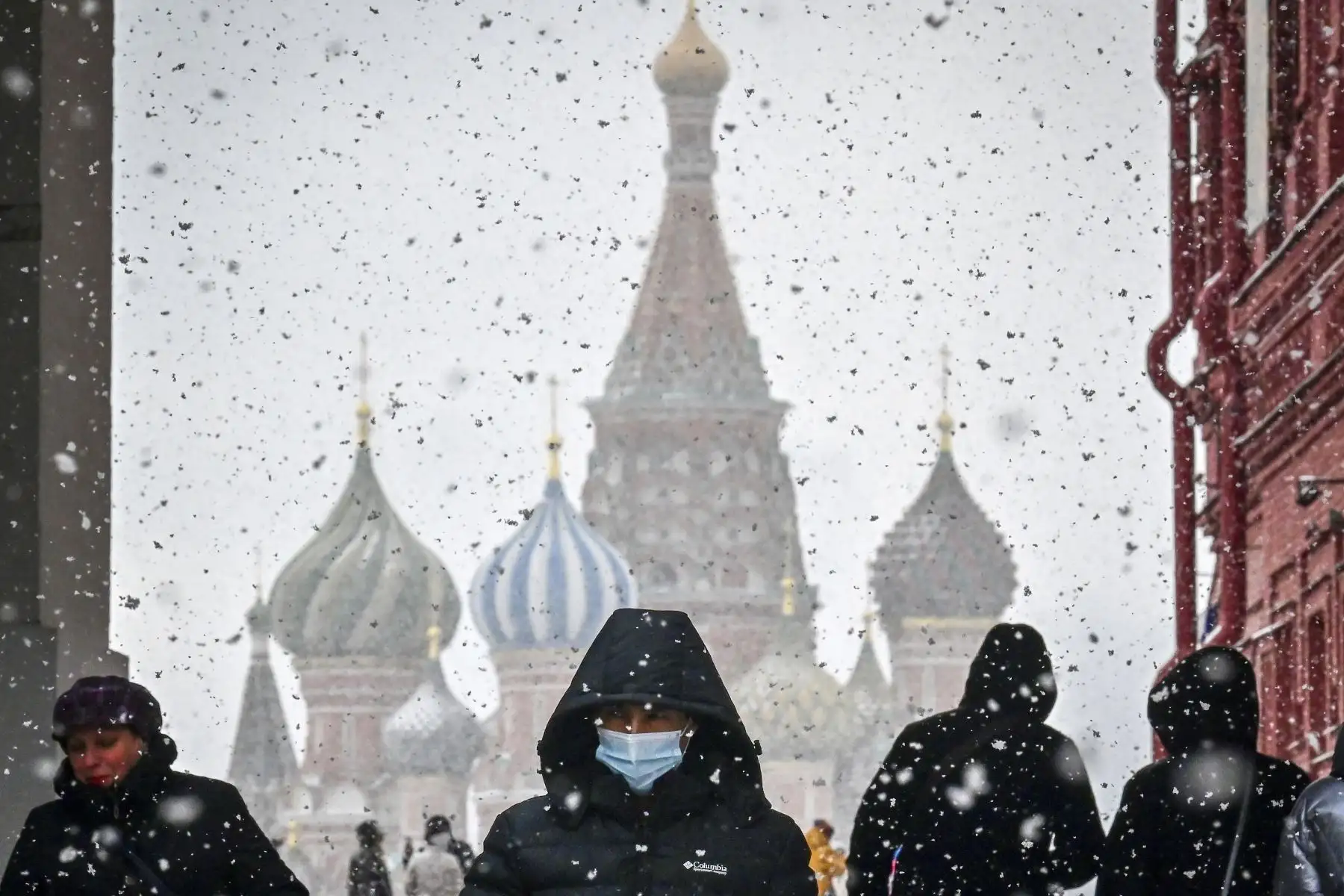 Un hombre que usa una mascarilla para protegerse contra la enfermedad Covid-19 camina por la Plaza Roja con la catedral de San Basilio durante la nevada sobre Moscú, en Rusia. Foto: AFP