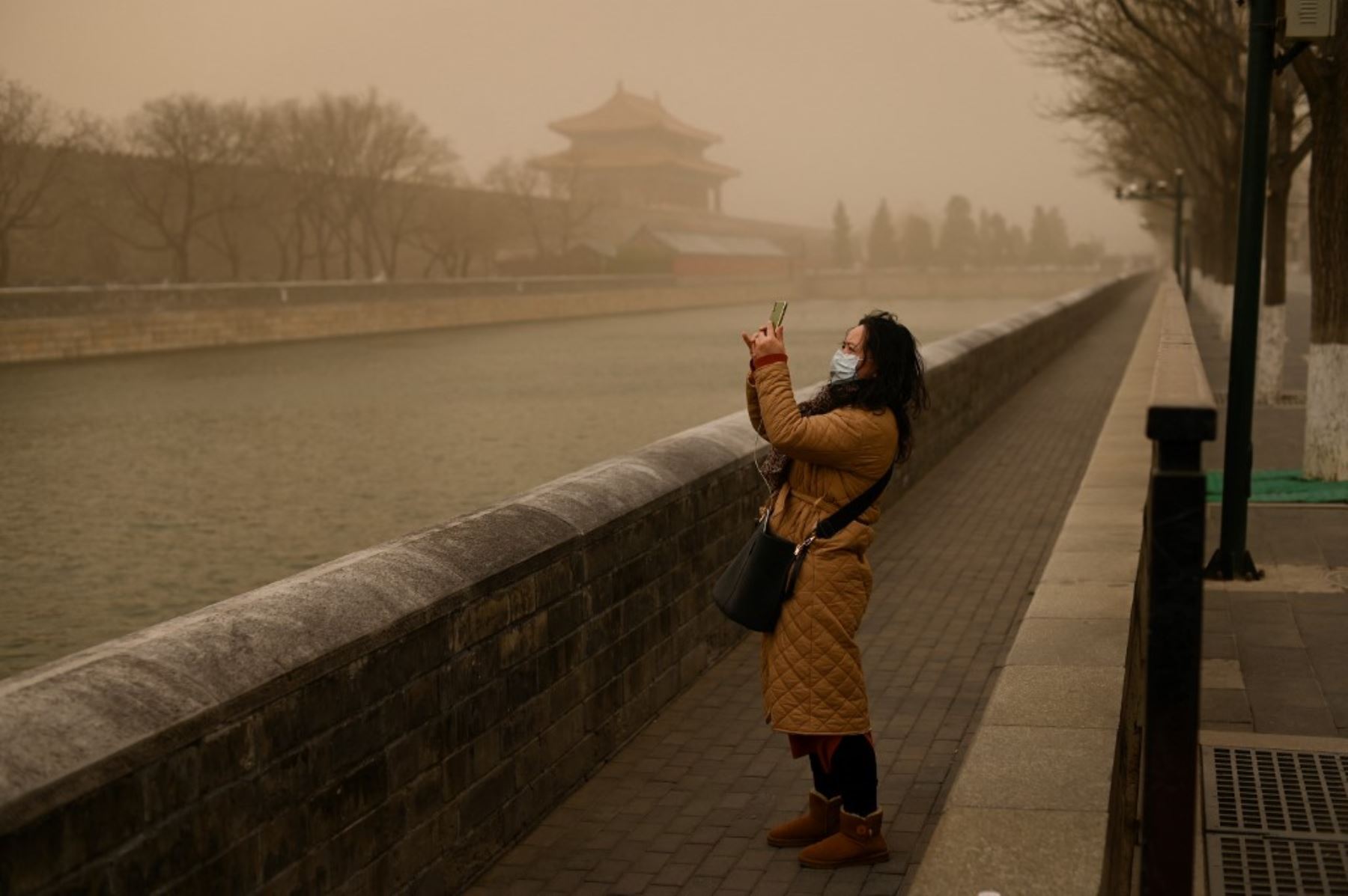 Una mujer usa un teléfono móvil para tomar fotografías fuera de la Ciudad Prohibida durante una tormenta de arena en Beijing.Foto: AFP