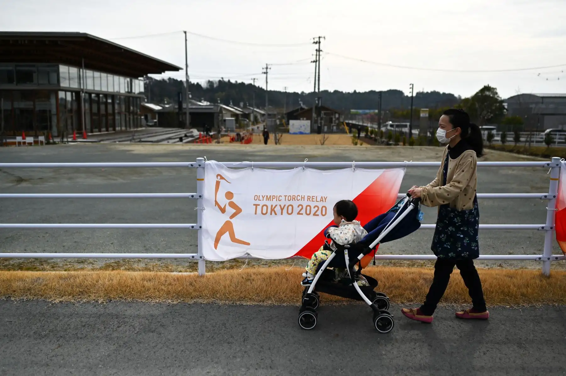 Una mujer empuja a un niño en un cochecito fuera de una sede del relevo de la antorcha el primer día del relevo de la antorcha olímpica de Tokio 2020 en la ciudad de Naraha, prefectura de Fukushima