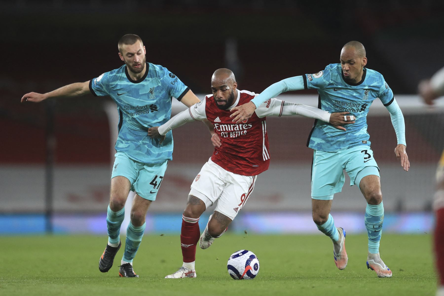 El delantero francés del Arsenal Alexandre Lacazette (C) detiene al defensor inglés del Liverpool Nathaniel Phillips (L) y al mediocampista brasileño del Liverpool Fabinho (R) durante el partido de fútbol de la Premier League inglesa entre el Arsenal y el Liverpool en el Emirates Stadium de Londres. Foto: AFP