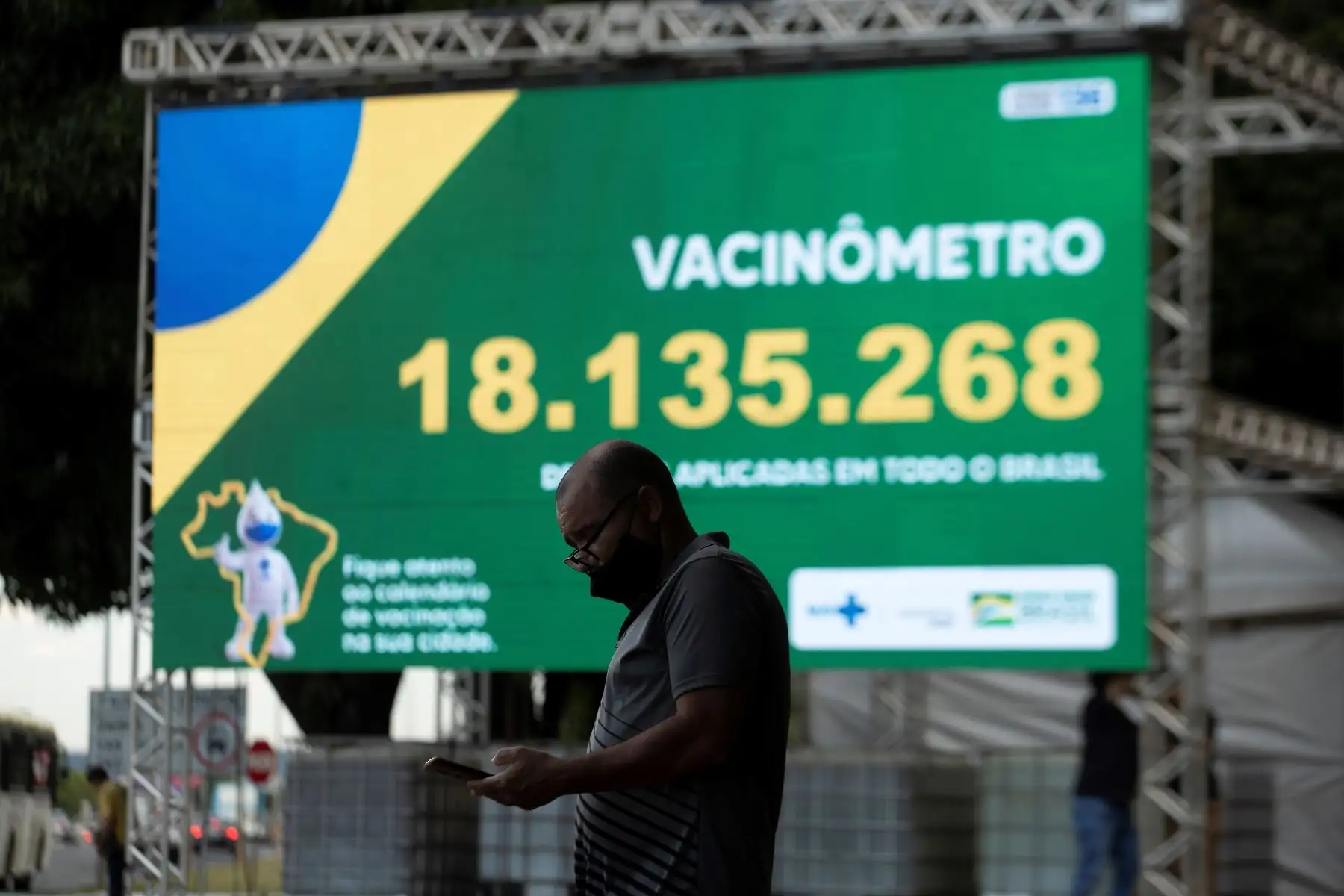 Un hombre observa su teléfono frente al "vacunómetro", un tablero digital donde se registra el número de personas vacunadas en Brasilia, el 30 de marzo del 2021. Foto: EFE