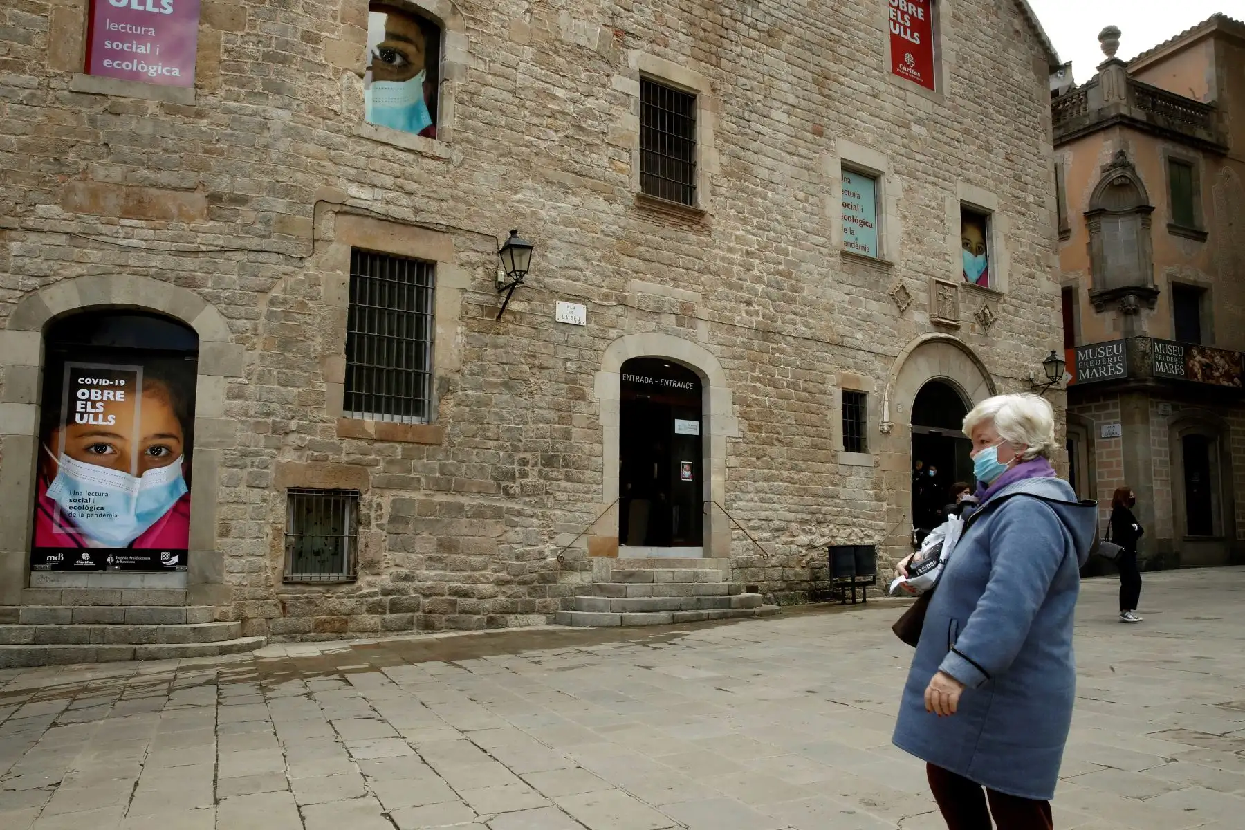 Una mujer pasa ante la sede del Museo Diocesano de Barcelona donde se expone "Abre los ojos: una lectura social y ecológica de la pandemia", que acerca las consecuencias sociales de la crisis de la COVID-19 a través una selección de imágenes y vídeos. Foto: EFE