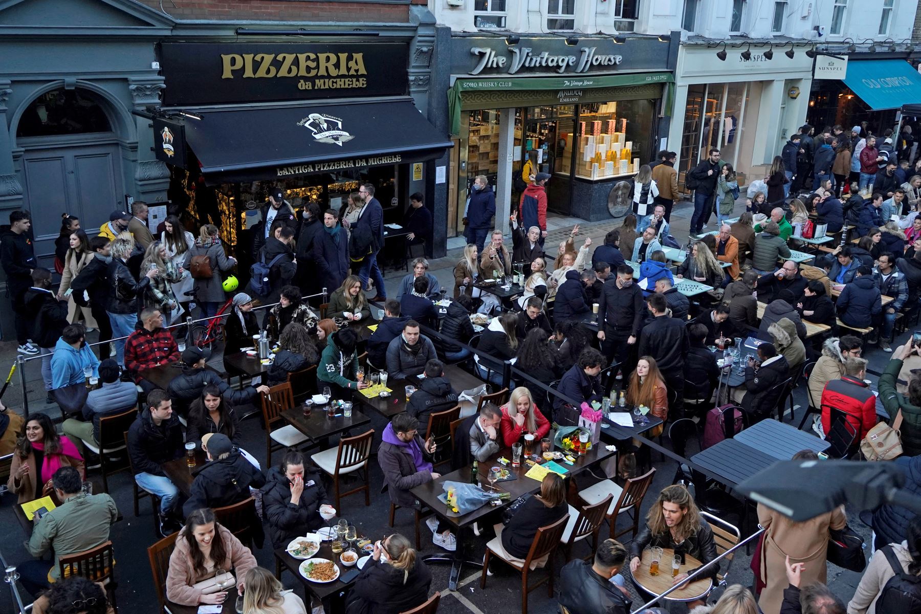 La gente se sienta en mesas al aire libre para comer y beber en bares y restaurantes reabiertos, en la calle en el área del Soho de Londres, el 16 de abril de 2021. Foto: AFP