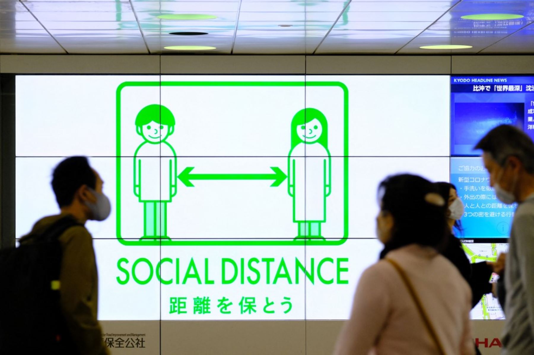 Personas que usan máscaras pasan frente a una exhibición de servicio público que promueve el distanciamiento social en una explanada que conduce a la estación terminal en el distrito Shinjuku de Tokio, bajo las medidas de cuasi-emergencia más recientes en medio de un aumento en los casos de coronavirus covid-19 en país. Foto: AFP