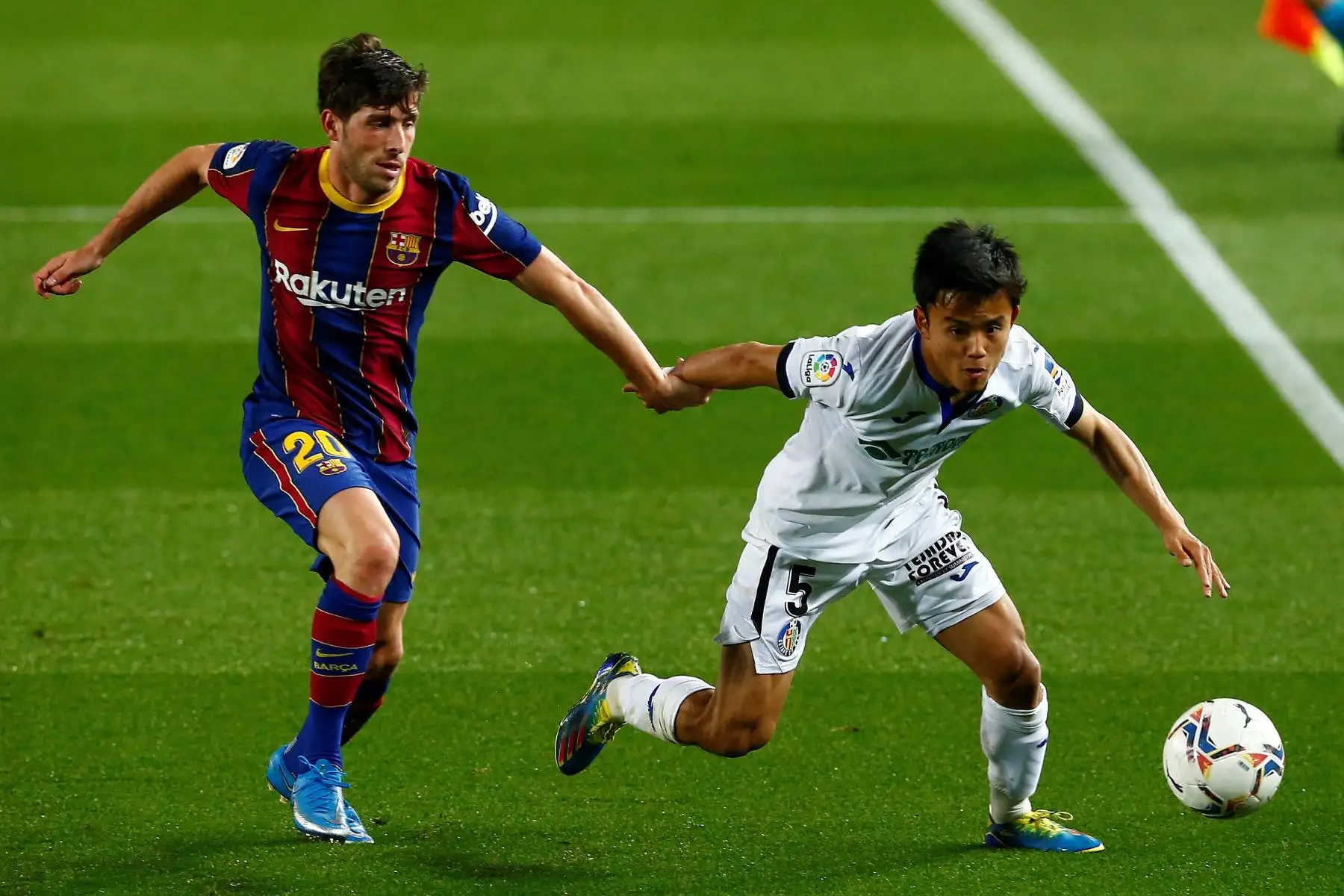 El centrocampista japonés del Getafe, Takefusa Kubo , conduce el balón ante la marca del centrocampista del FC Barcelona, ​​Sergi Roberto, durante partido disputado por la Liga española. Foto: EFE