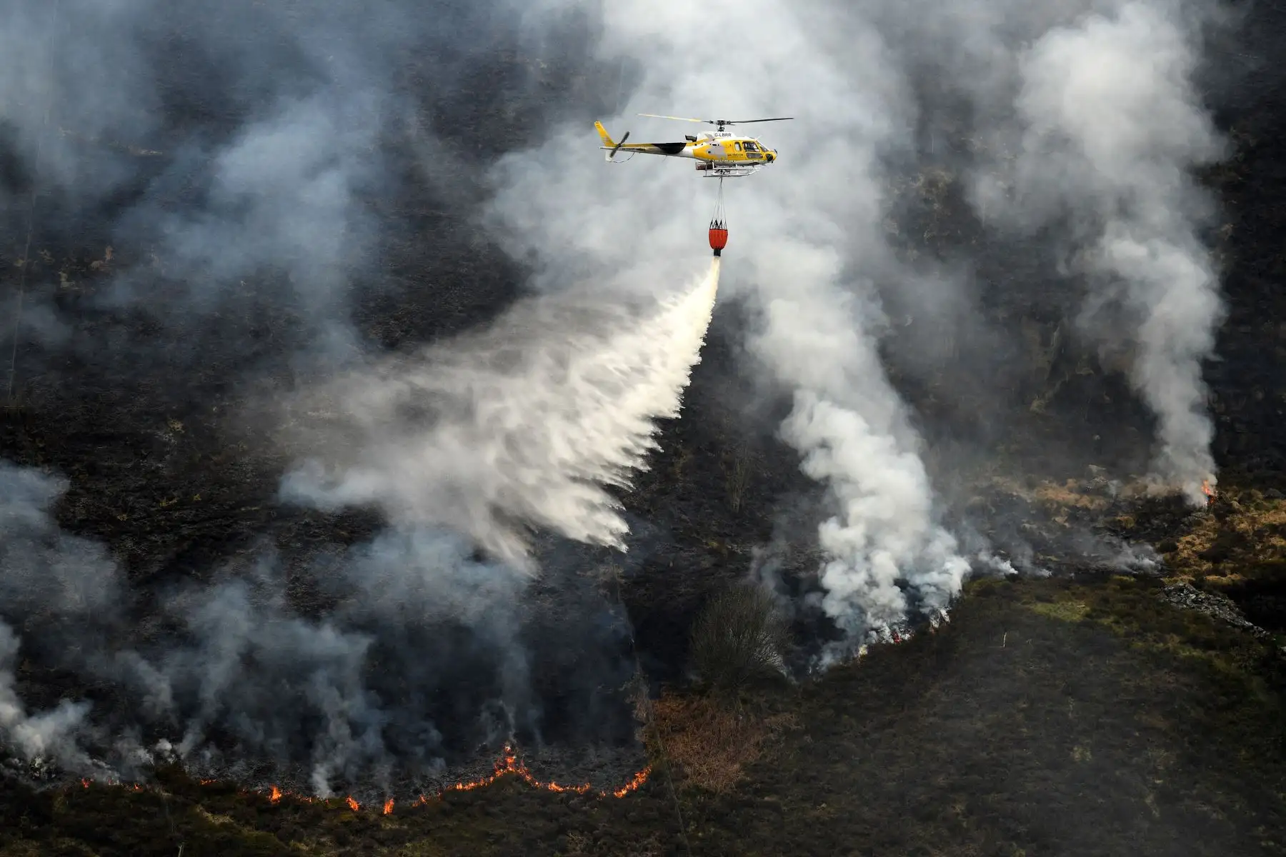 Un helicóptero arroja agua, tomada de un embalse cercano, después del resurgimiento del incendio del páramo en Marsden Moor, cerca de Huddersfield, en el norte de Inglaterra, el 27 de abril de 2021. Foto: AFP