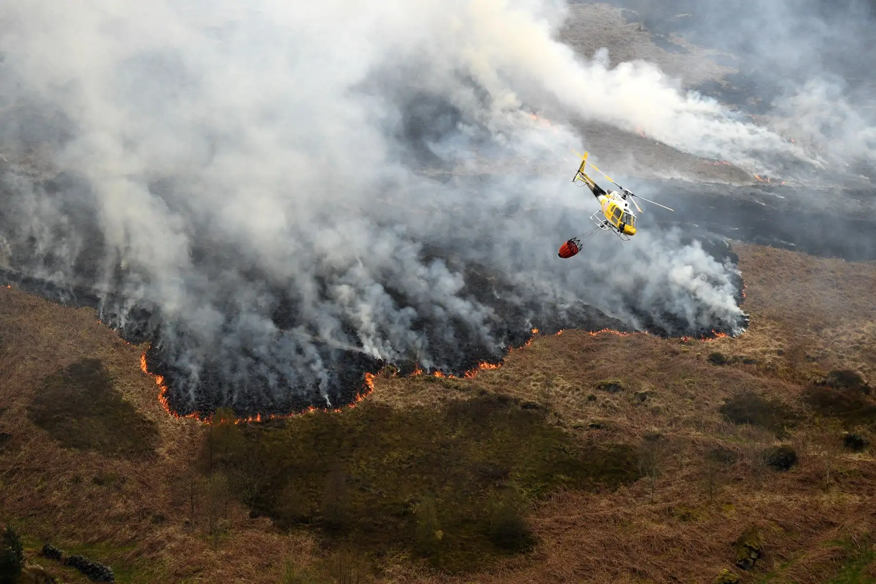 Un helicóptero arroja agua, tomada de un embalse cercano, después del resurgimiento del incendio del páramo en Marsden Moor, cerca de Huddersfield, en el norte de Inglaterra, el 27 de abril de 2021. Foto: AFP